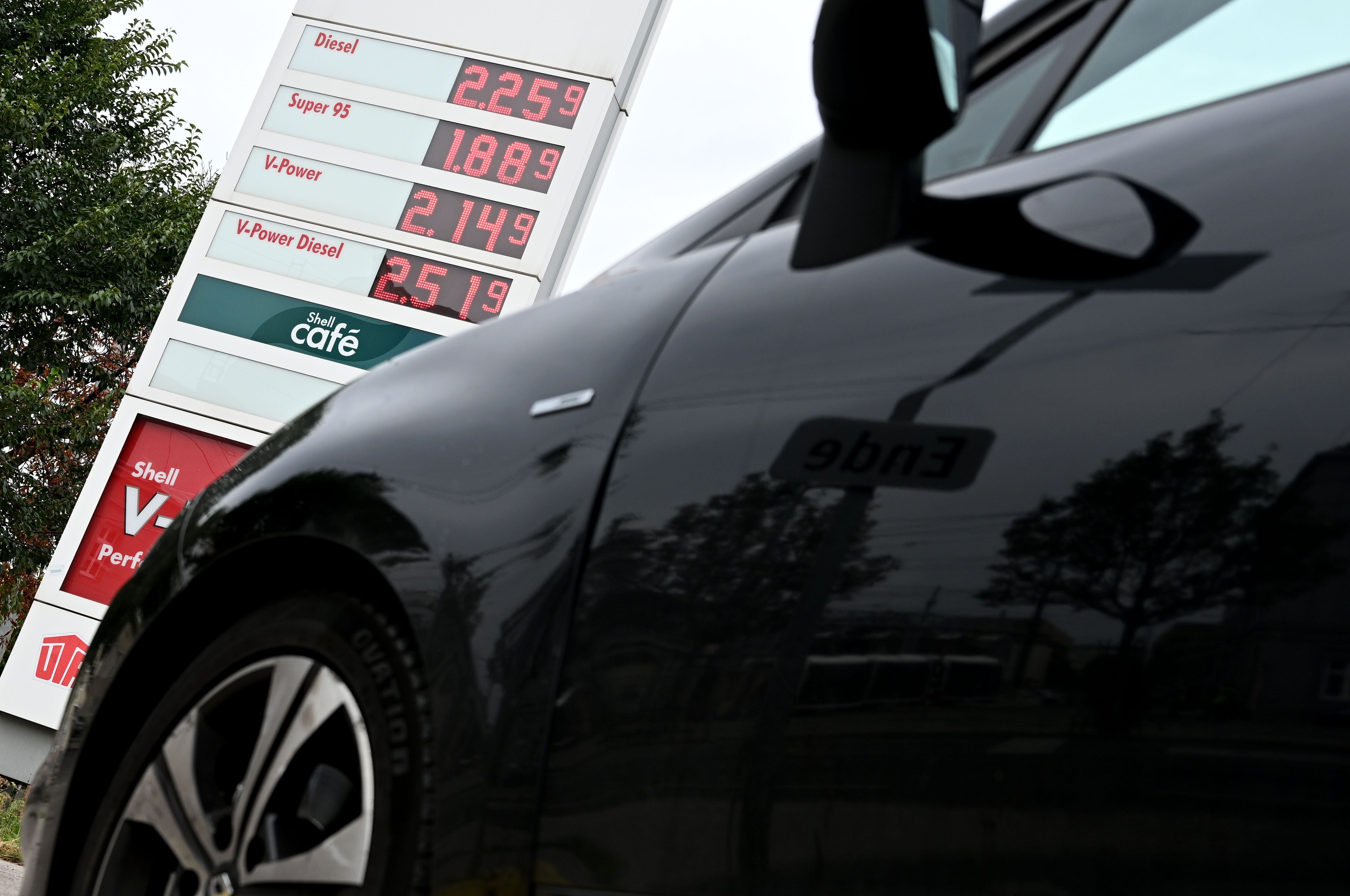 Ein schwarzes Auto vor einer Anzeigetafel mit aktuellen Spritpreisen an einer Tankstelle in Wien.