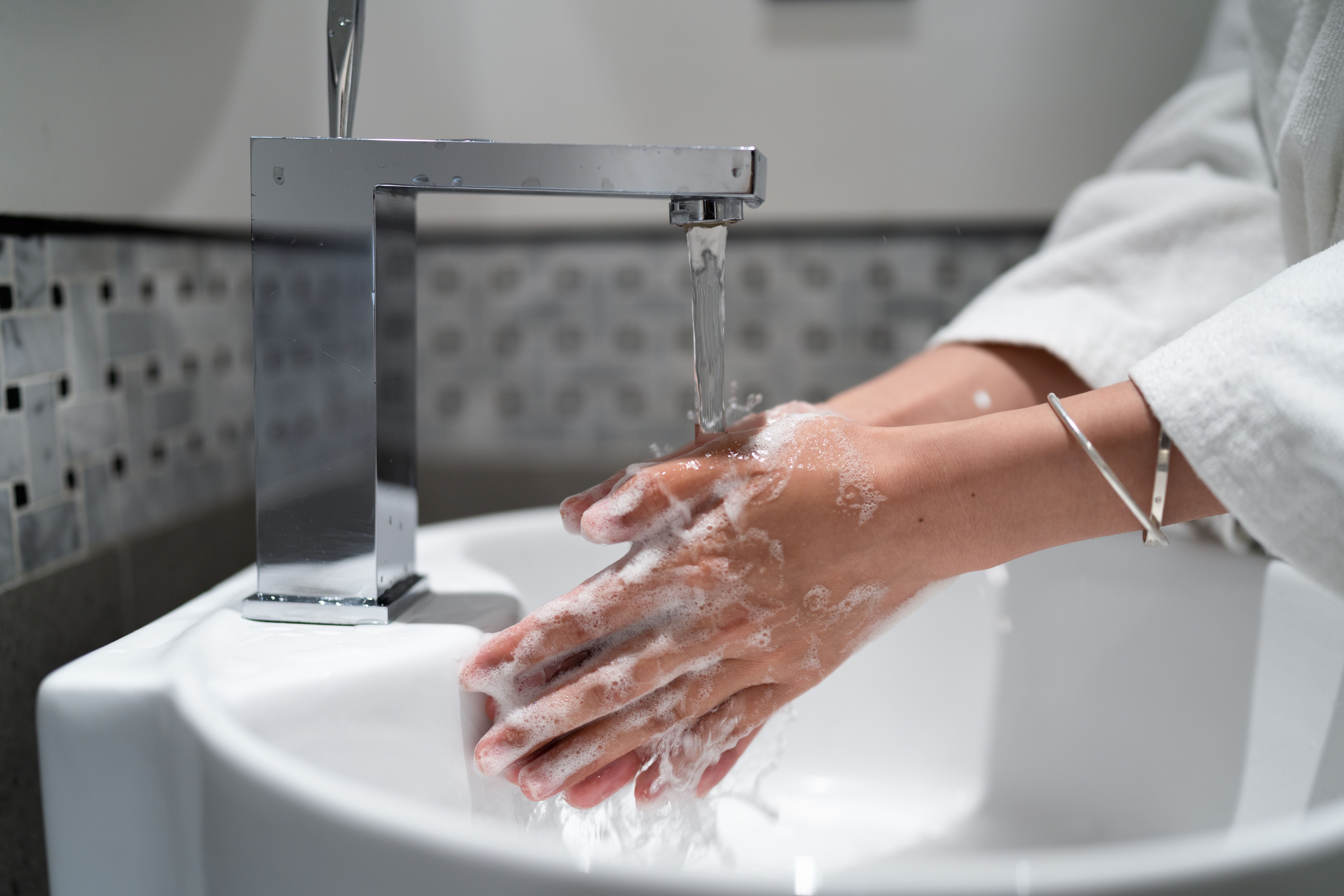 Hände werden mit Seife unter fließendem Wasser an einem modernen Waschbecken gewaschen.