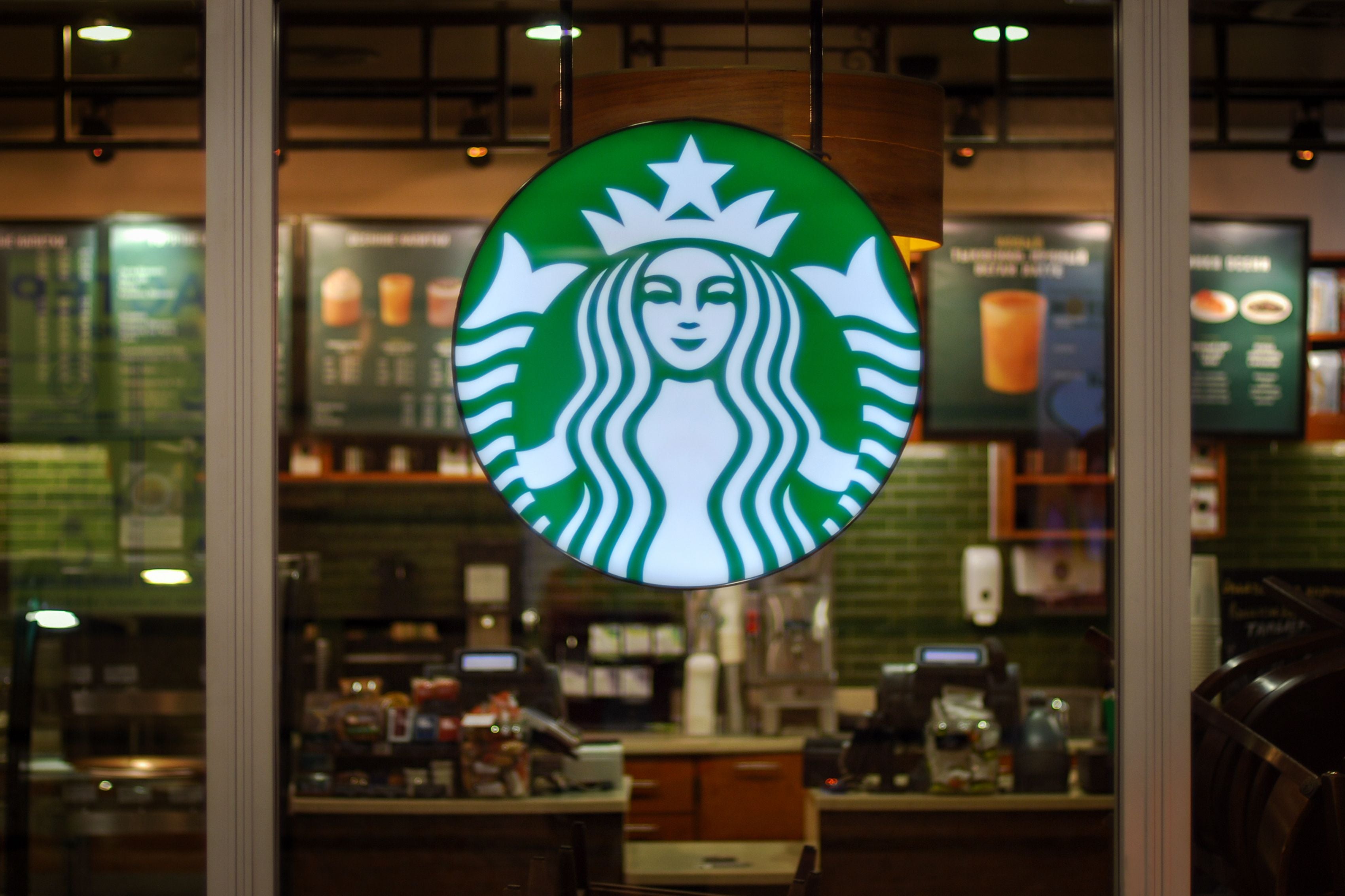 Leuchtendes Starbucks-Logo vor einem leeren Café-Innenraum hinter einer Glaswand.