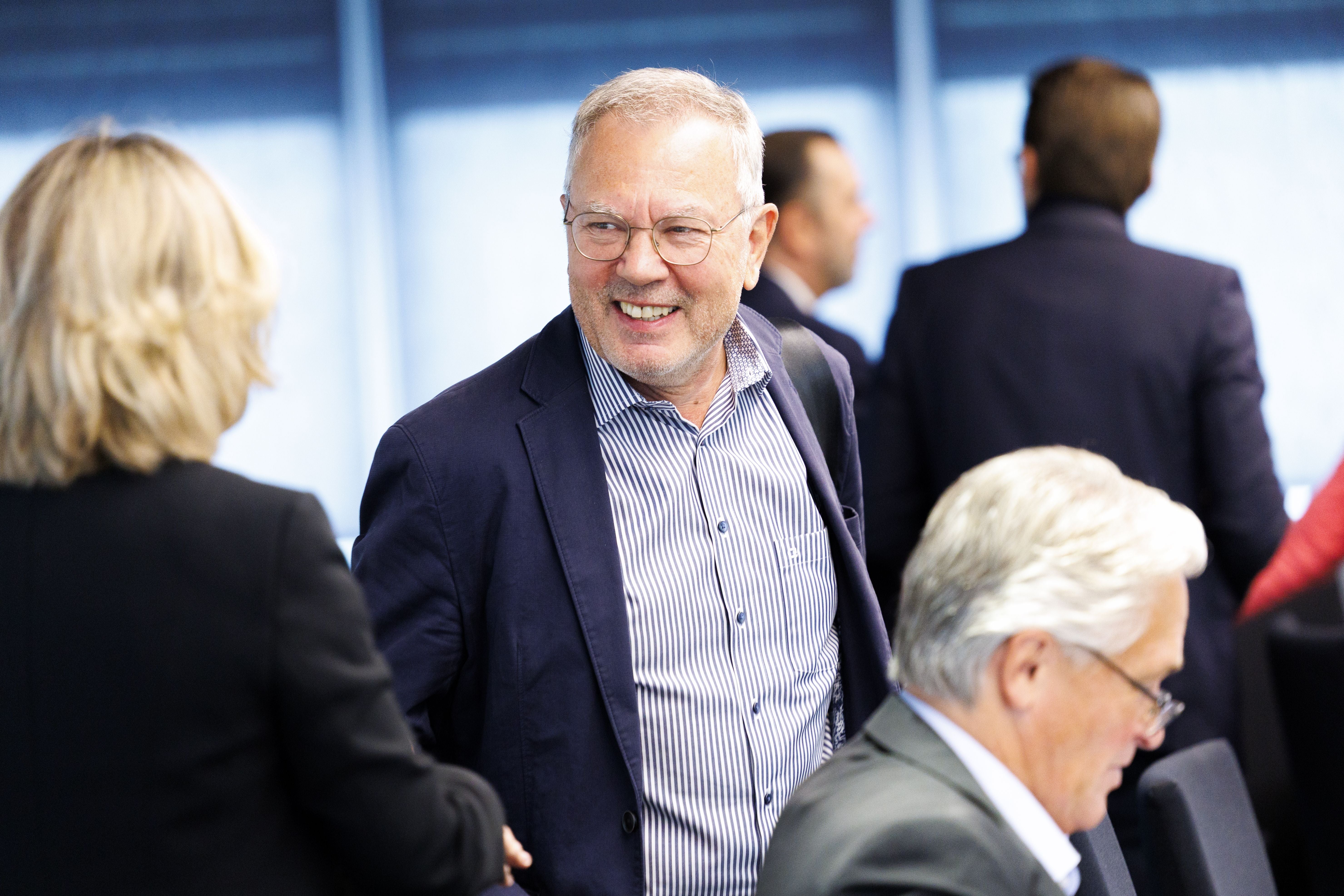 Ein älterer Mann im Anzug lächelt in einem Konferenzraum und spricht mit einer Frau.