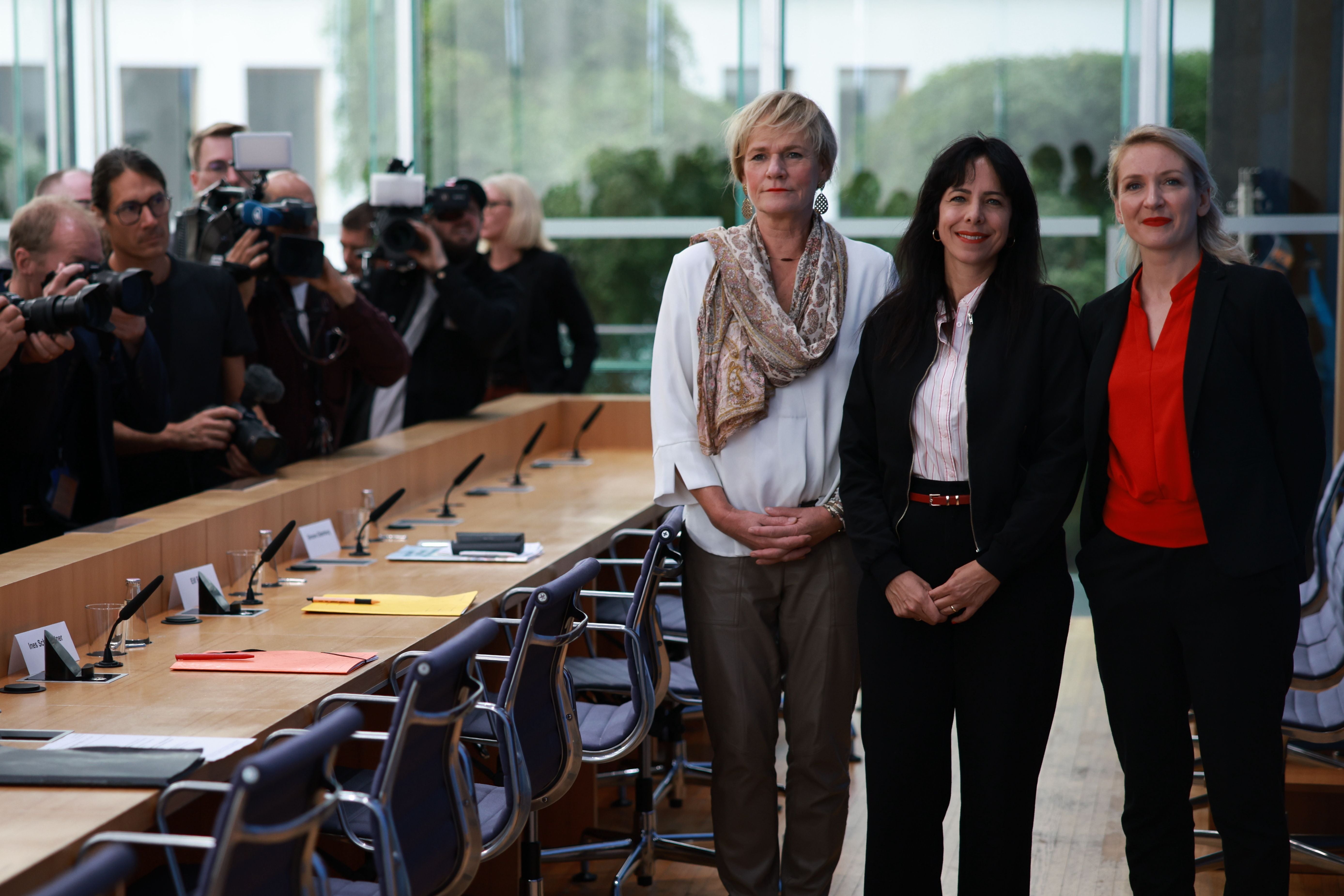 Drei Frauen posieren vor Pressefotografen in einem modernen Konferenzraum in Berlin.
