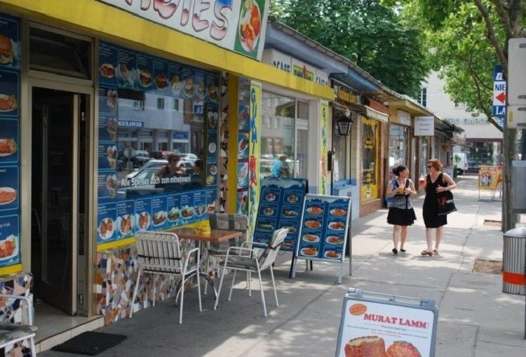 Zwei Frauen gehen an Imbissbuden mit Außentischen am Nussdorfer Markt vorbei.