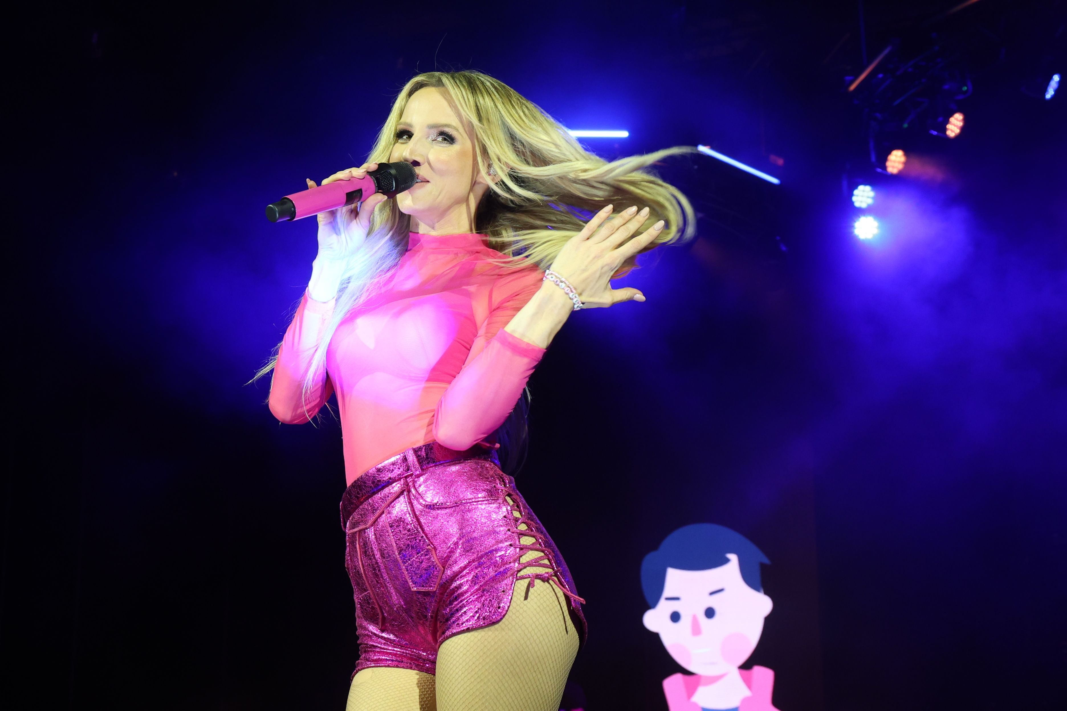 Sängerin in pinkem Outfit singt mit Mikrofon auf Bühne, lila Licht im Hintergrund.