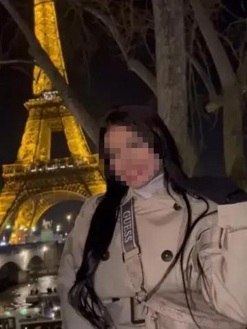 Frau mit langem Haar vor beleuchtetem Eiffelturm bei Nacht.