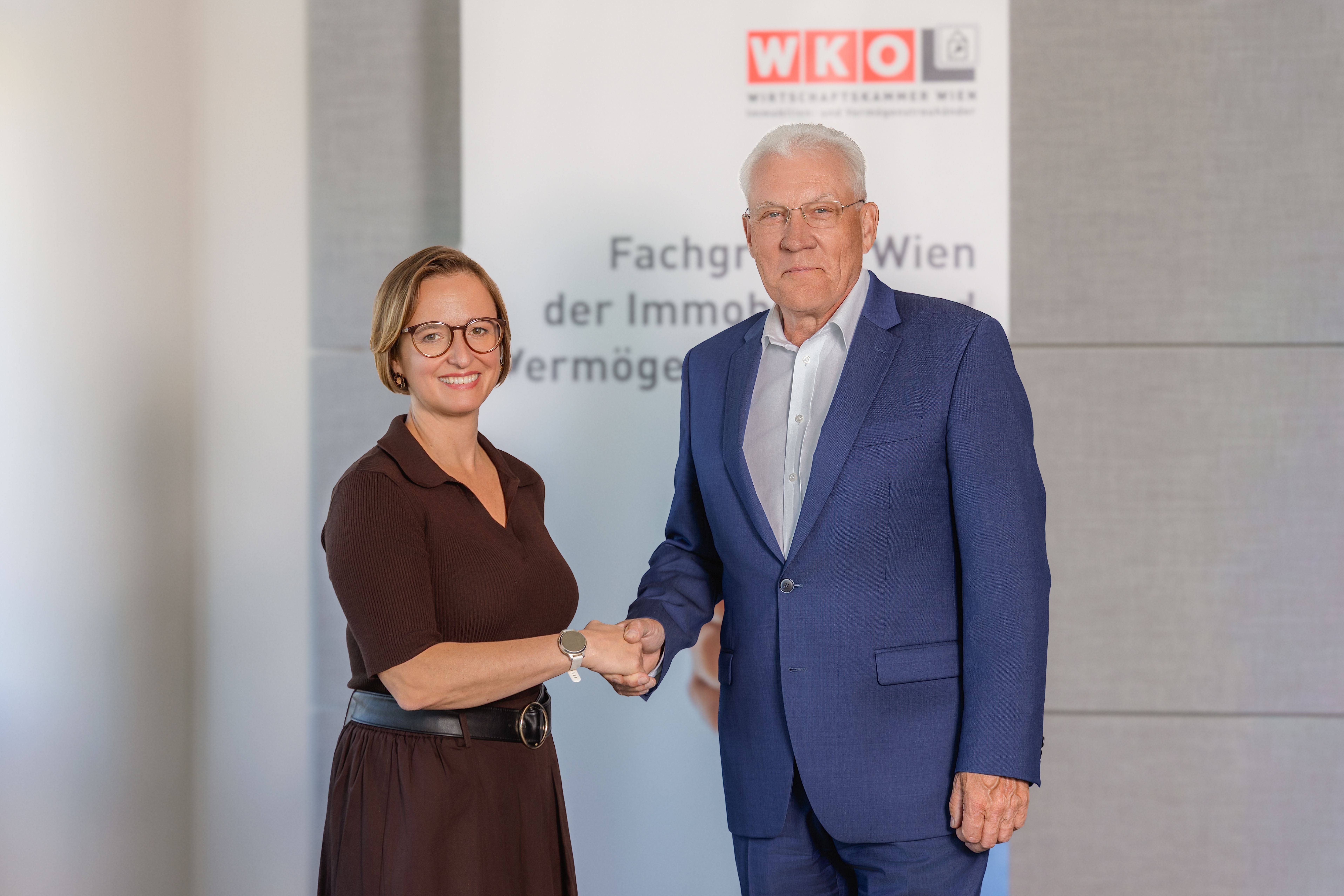Eine Frau und ein Mann geben sich vor einem WKO-Banner die Hand und lächeln in die Kamera.