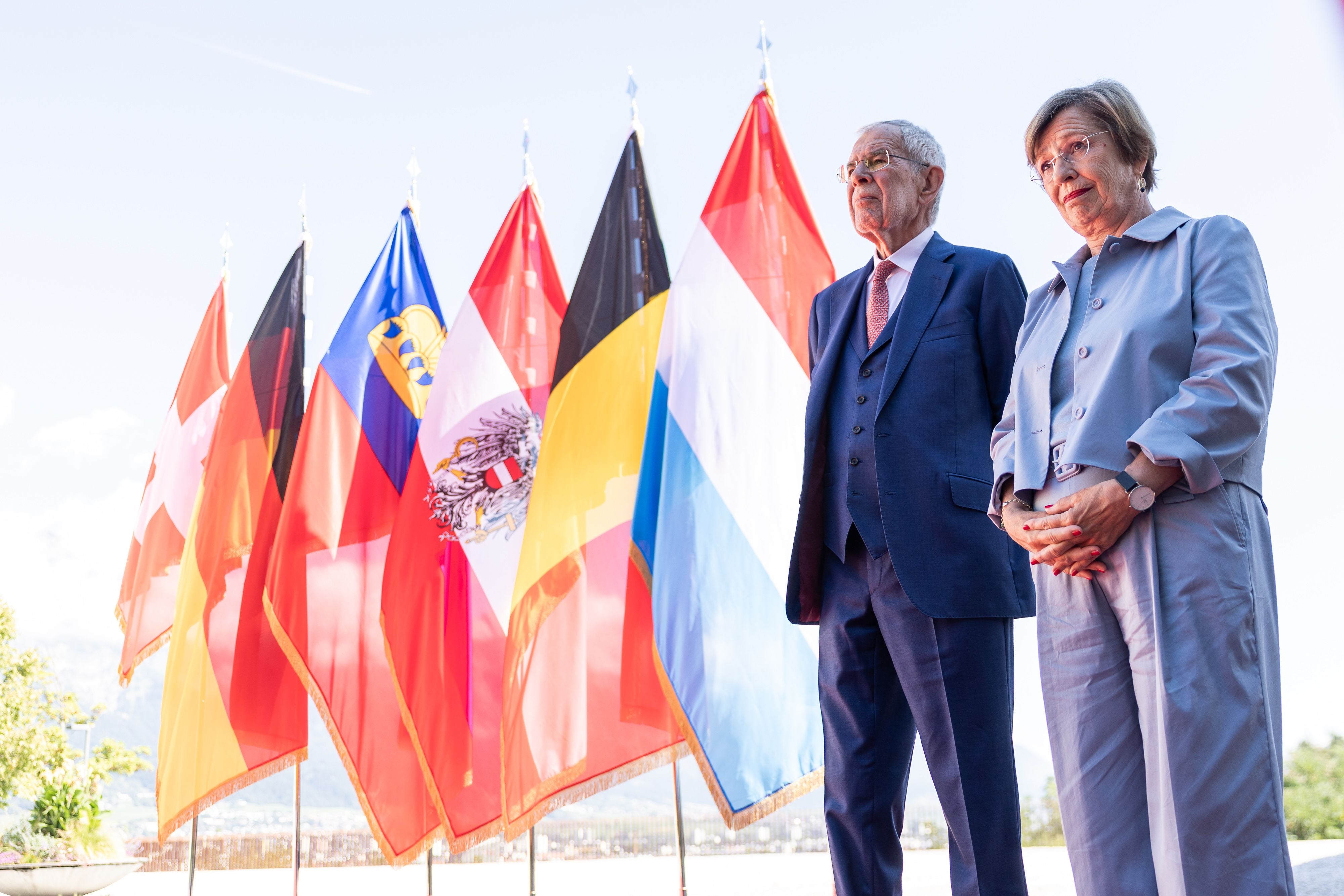 Ein Mann und eine Frau stehen vor mehreren europäischen Nationalflaggen im Freien.