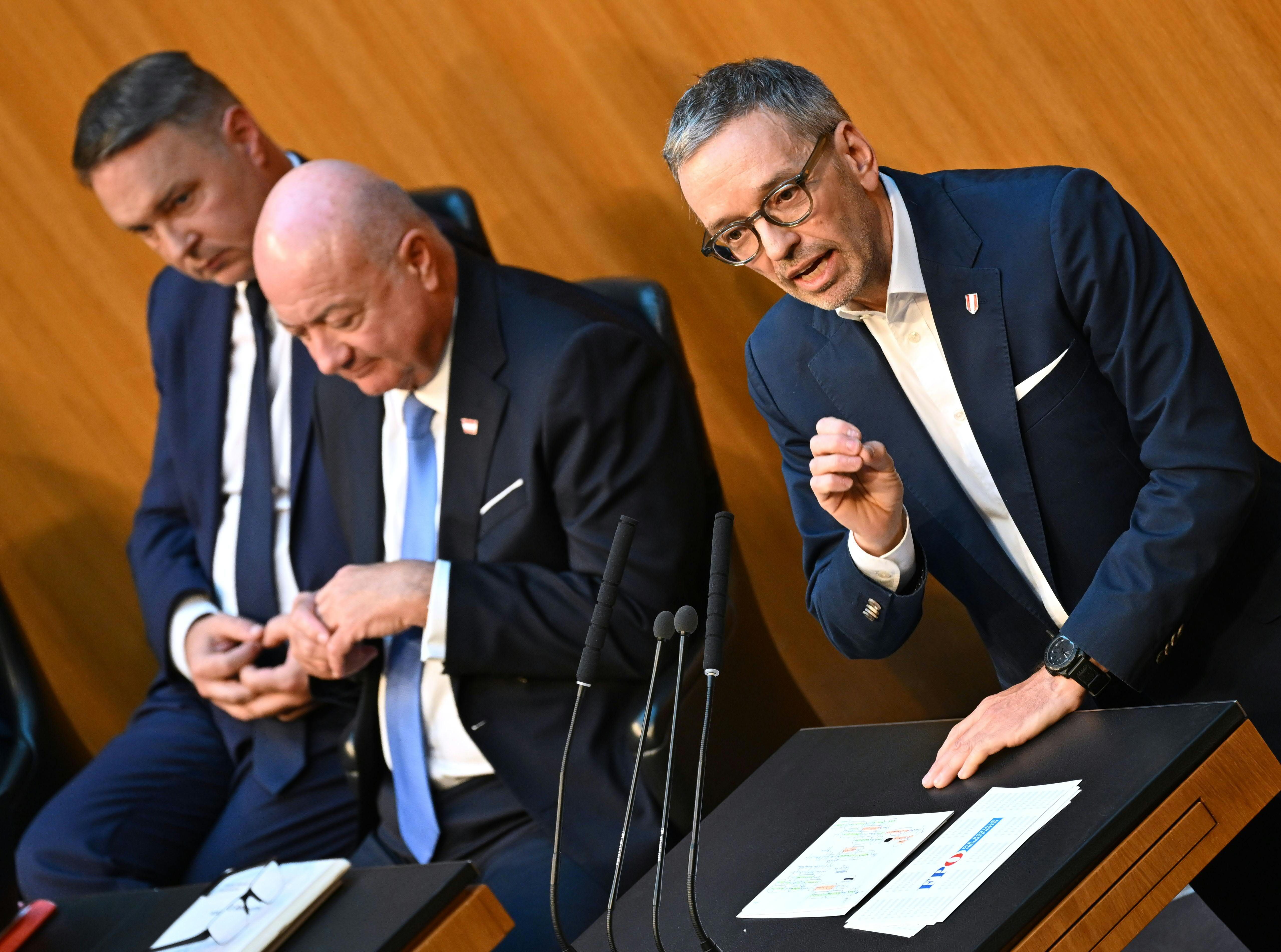 Drei Männer im Anzug bei einer Sitzung im Nationalrat, einer spricht am Rednerpult.
