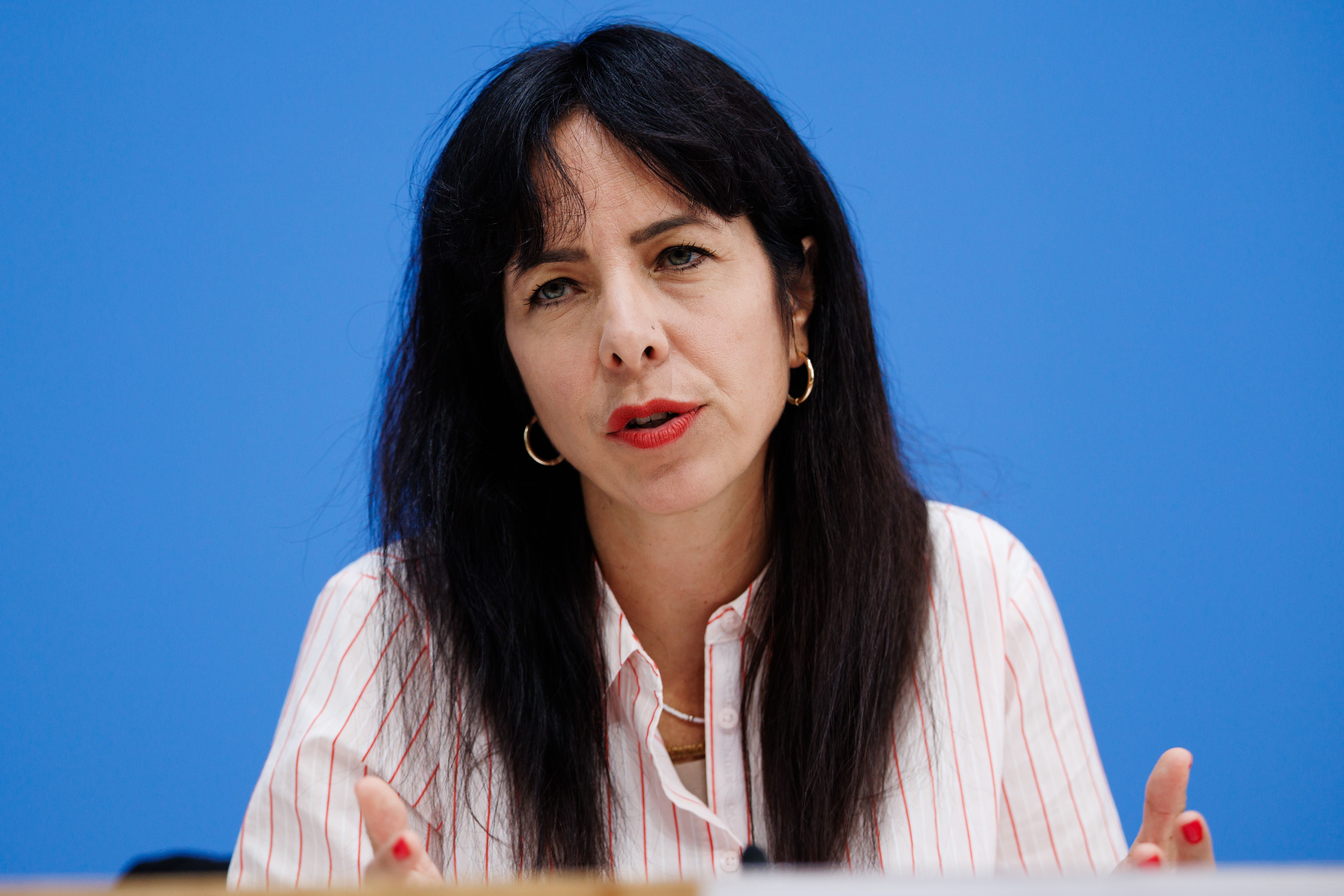 Eine Frau mit dunklen Haaren spricht vor blauem Hintergrund bei einer Pressekonferenz.