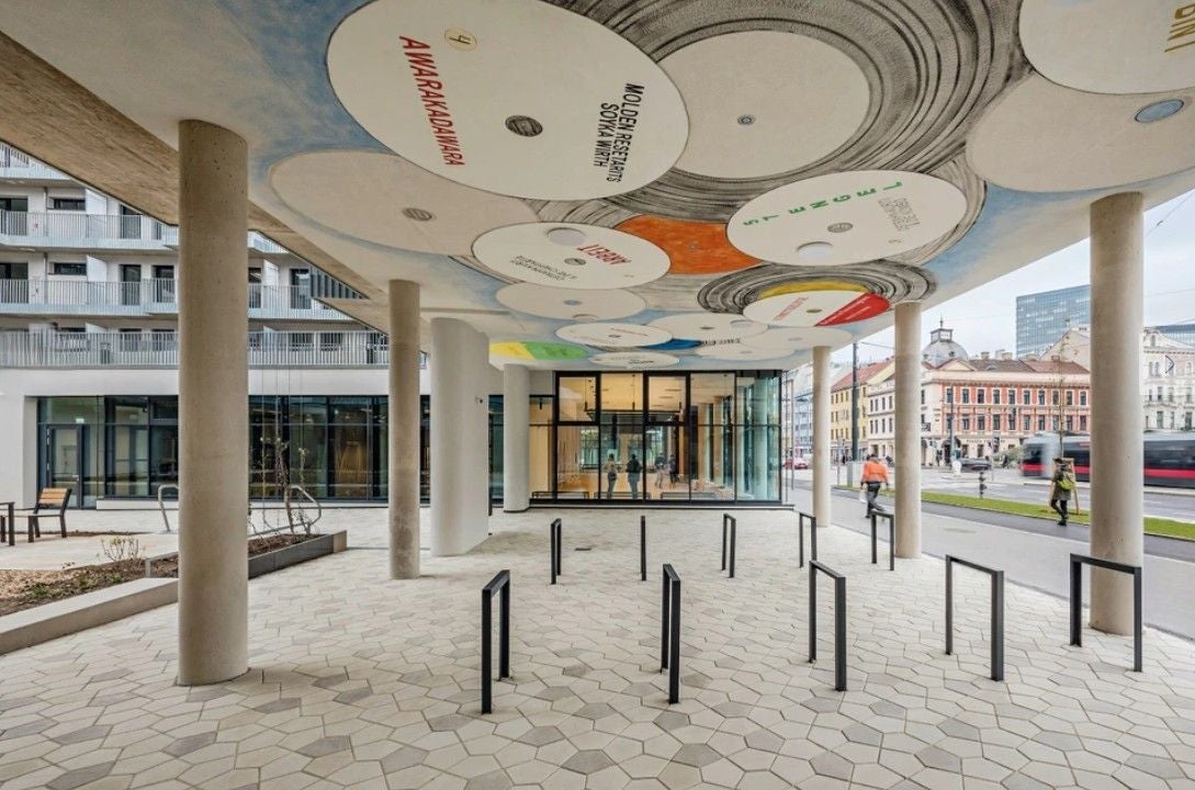 Moderner Innenhof mit Säulen, bunter Deckengestaltung und Fahrradständern im Willi-Resetarits-Hof.