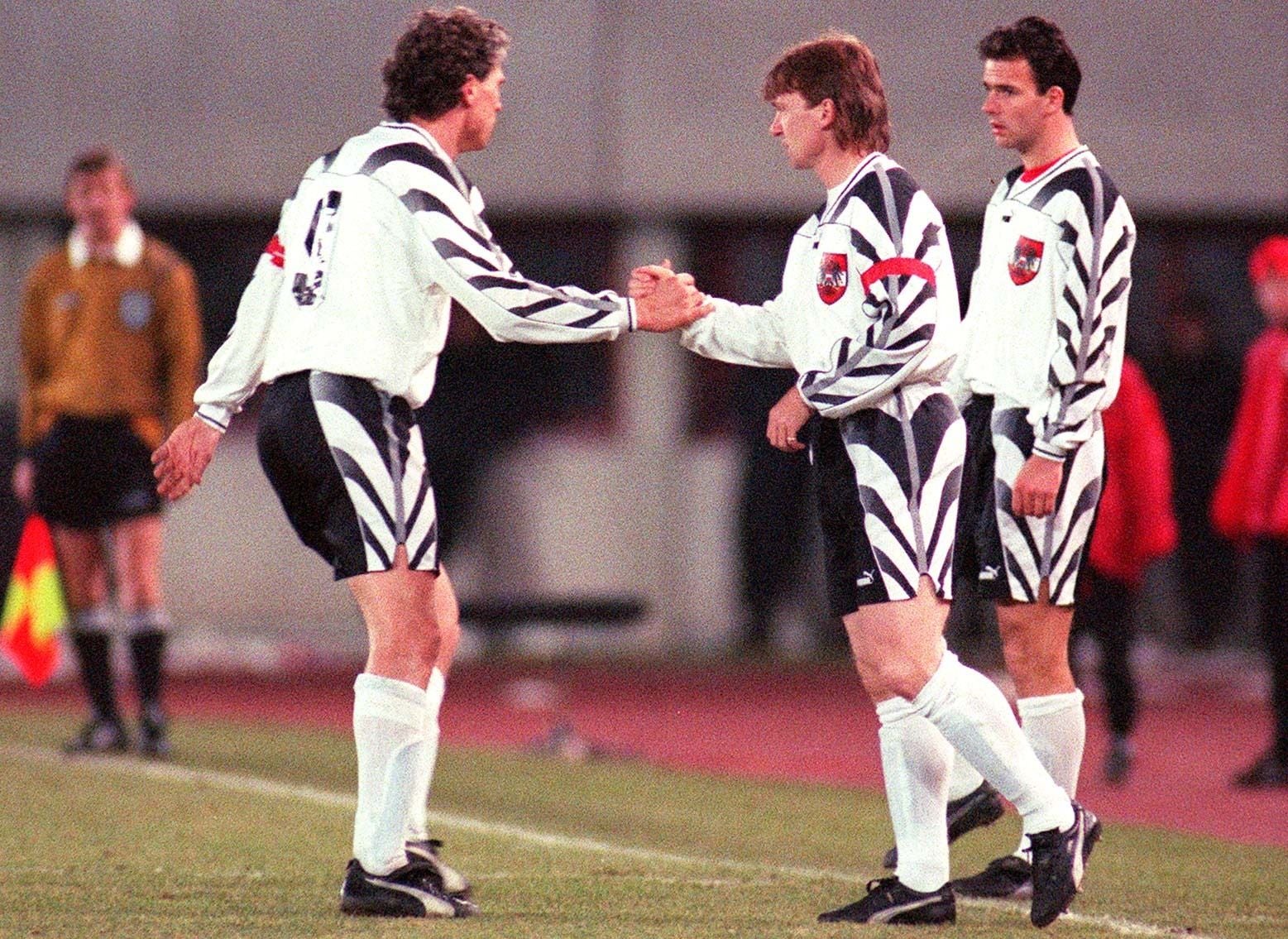 Andreas Ogris schüttelt Toni Polster am Spielfeldrand im ÖFB-Trikot die Hand, während Mario Haas danebensteht.