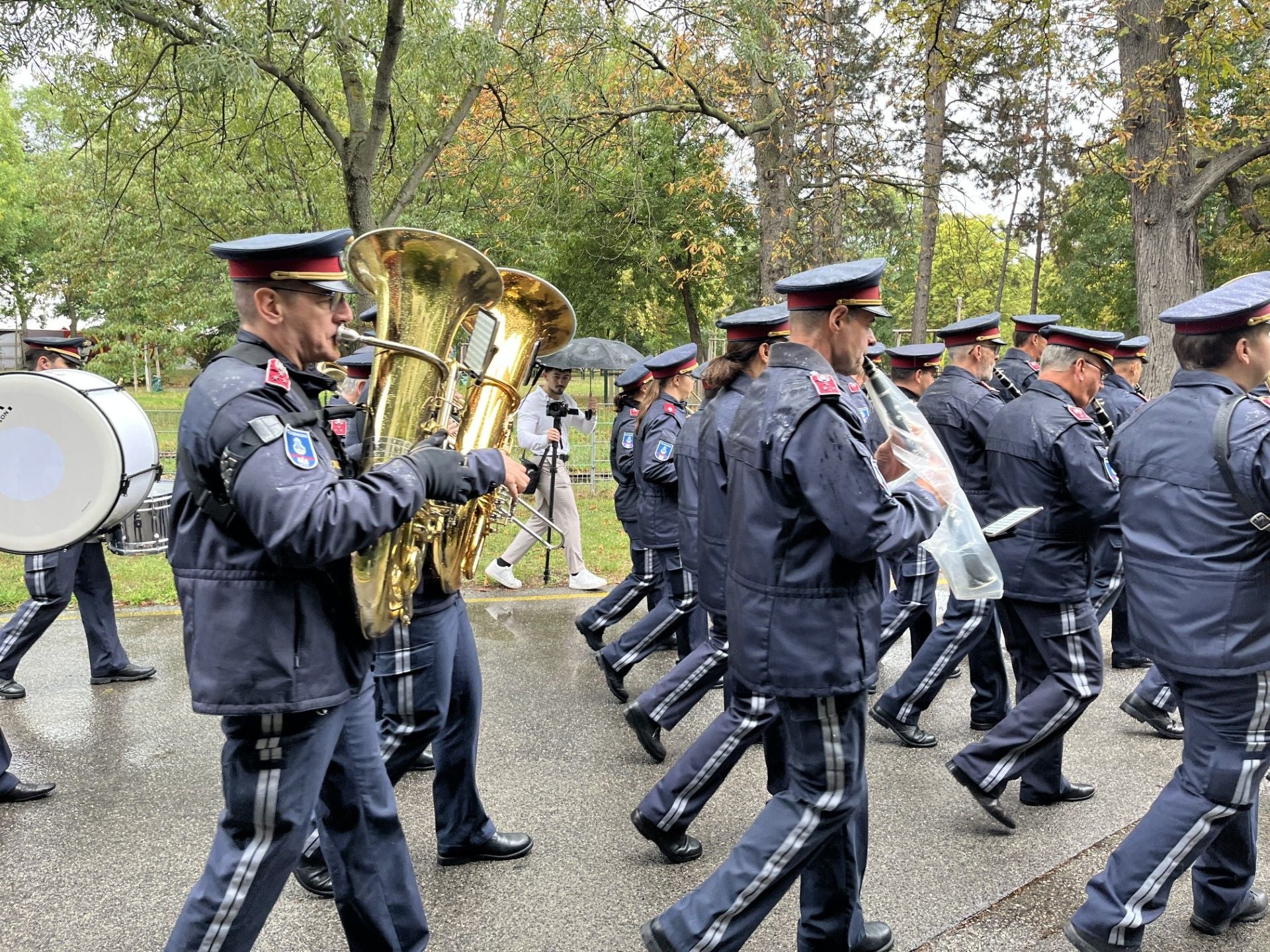 Eine Polizeikapelle marschiert im Freien und spielt Instrumente bei regnerischem Wetter.