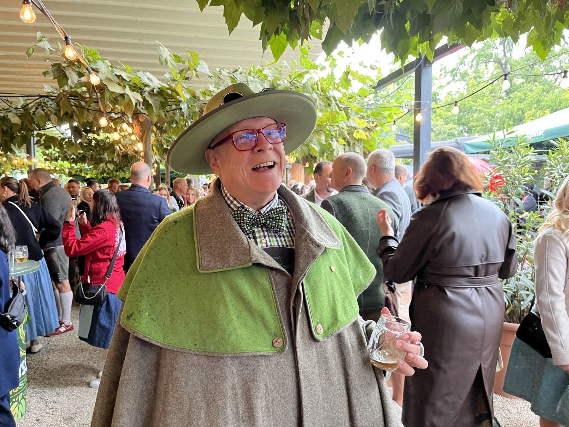 Ein Mann im traditionellen Gewand mit Hut hält ein Bierglas auf einem Volksfest.