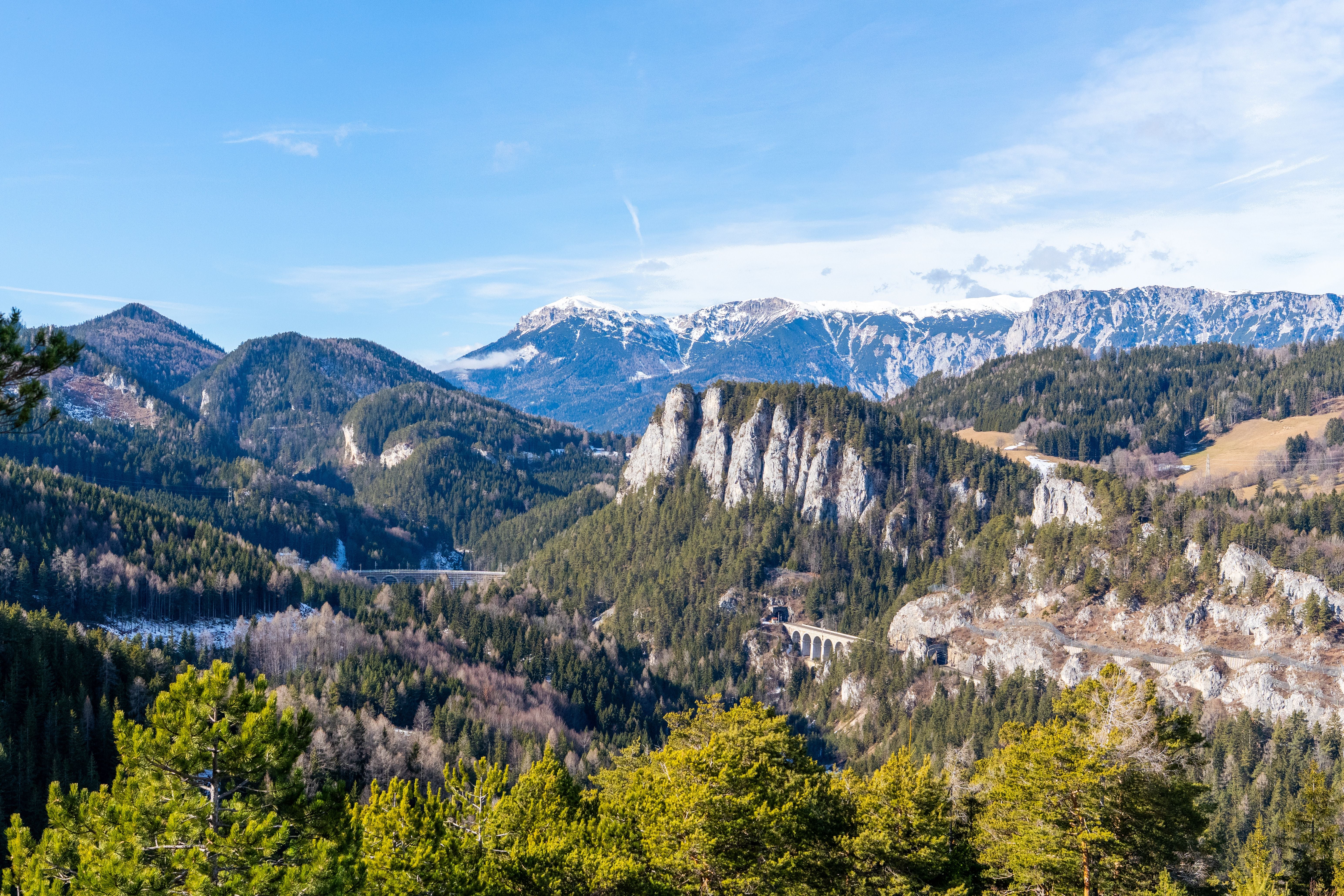 Weitblick auf bewaldete Alpen, felsige Berge und eine historische Eisenbahnbrücke bei Semmering in Österreich.