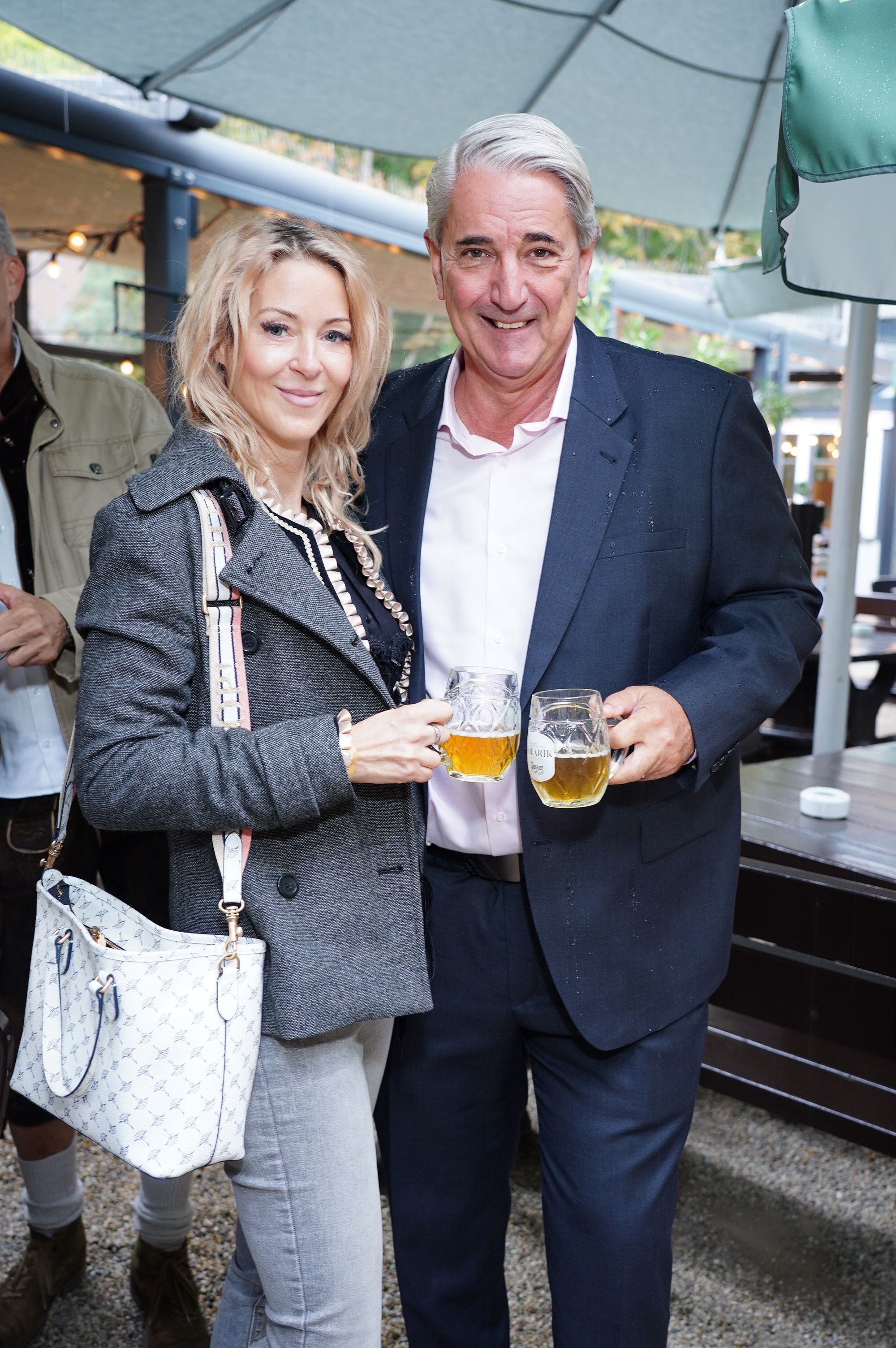 Ein Mann und eine Frau stoßen auf der Wiener Kaiser Wiesn im Freien mit Biergläsern an.