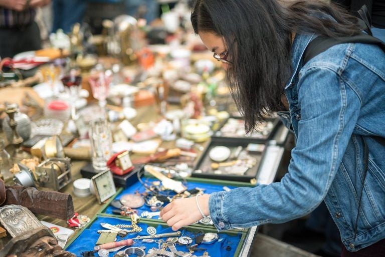 Eine Frau betrachtet Schmuck und Kleinigkeiten auf einem bunten Flohmarktstand.