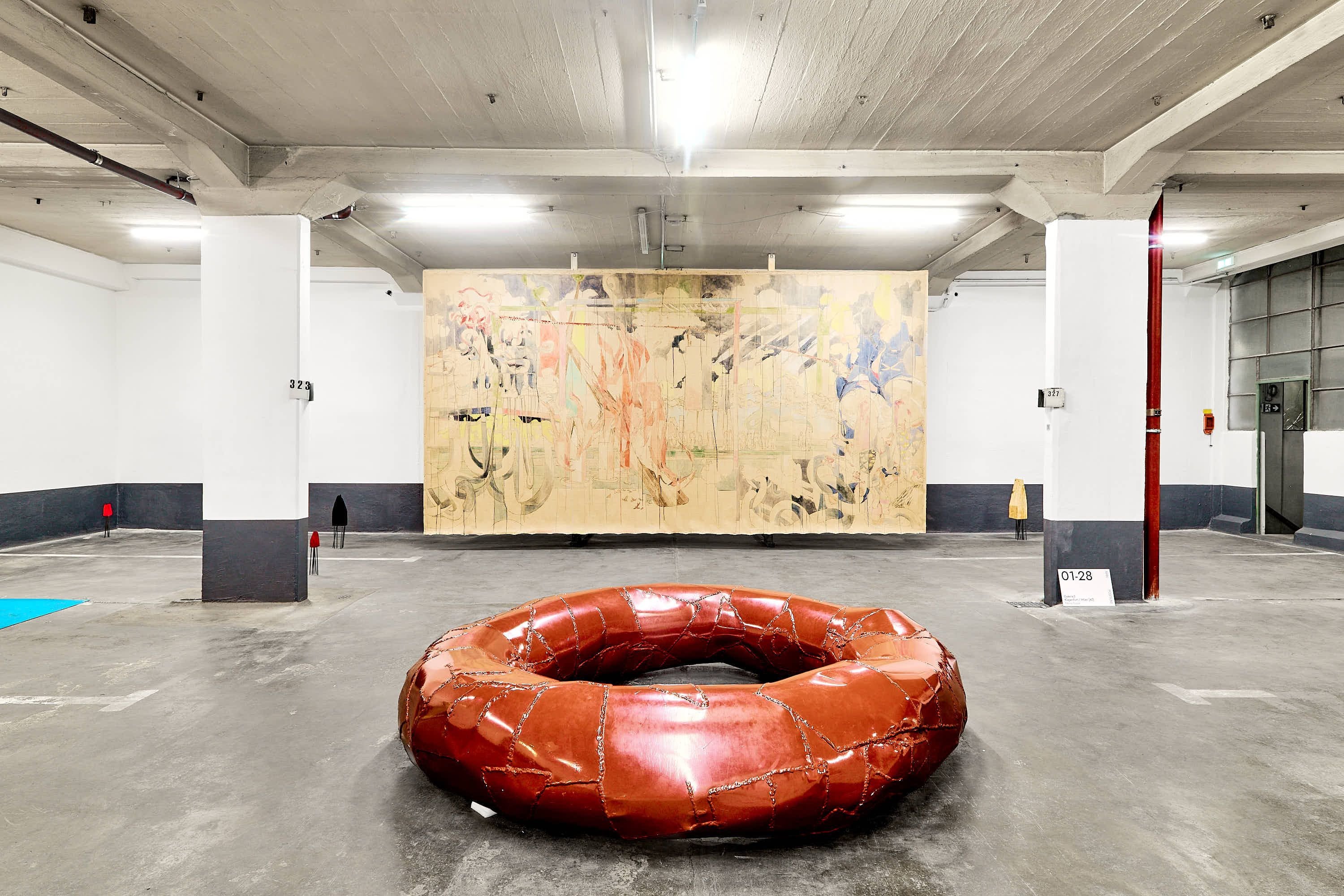 Kunstinstallation in heller Garage mit großem braunen Ringobjekt und abstraktem Gemälde an der Wand.
