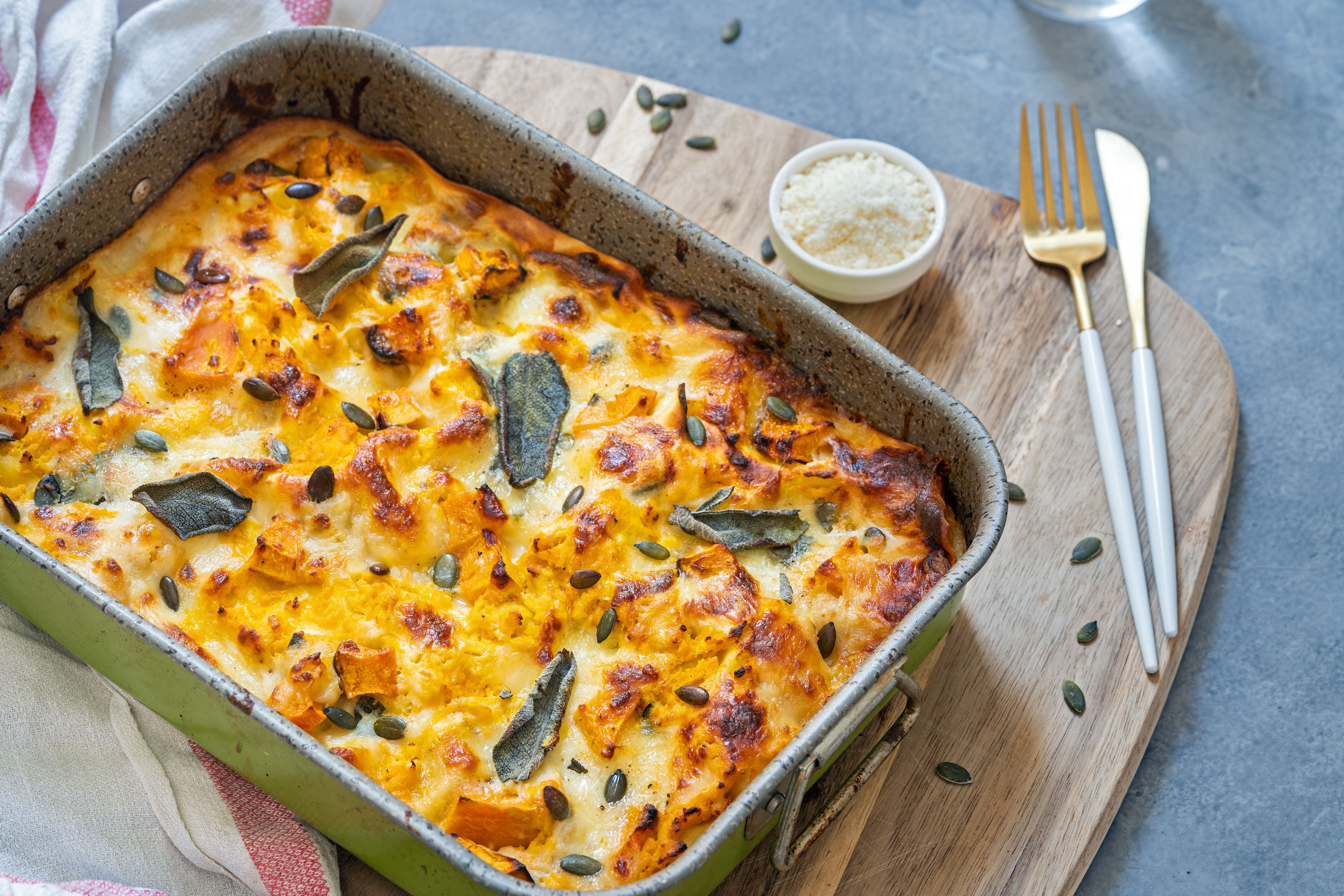Ofenfrische Kürbislasagne mit knuspriger Käsekruste, Salbeiblättern und Kürbiskernen in einer Auflaufform.