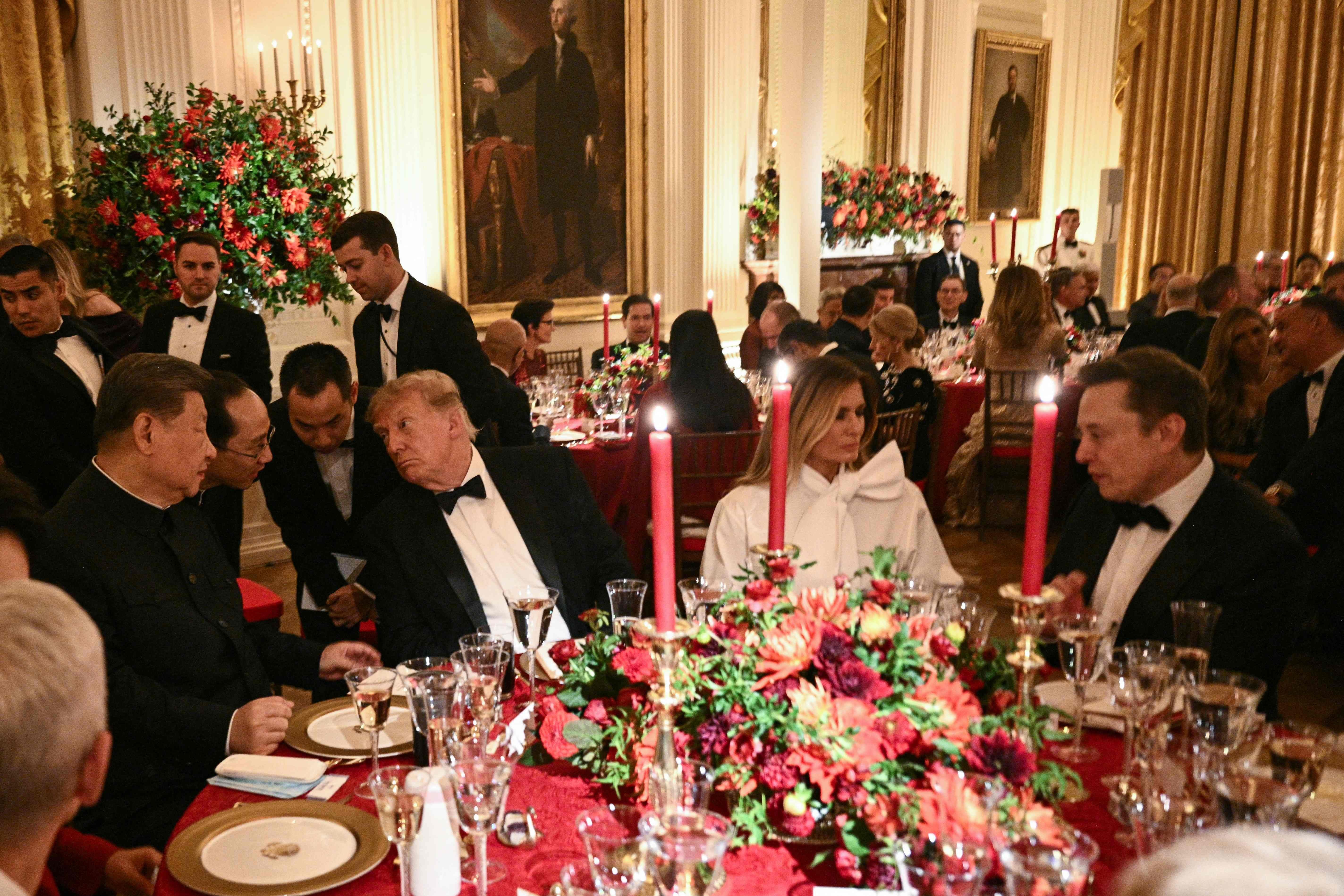 Festliches Staatsdinner mit Gästen im Anzug und Abendkleidern an reich gedeckten Tischen.