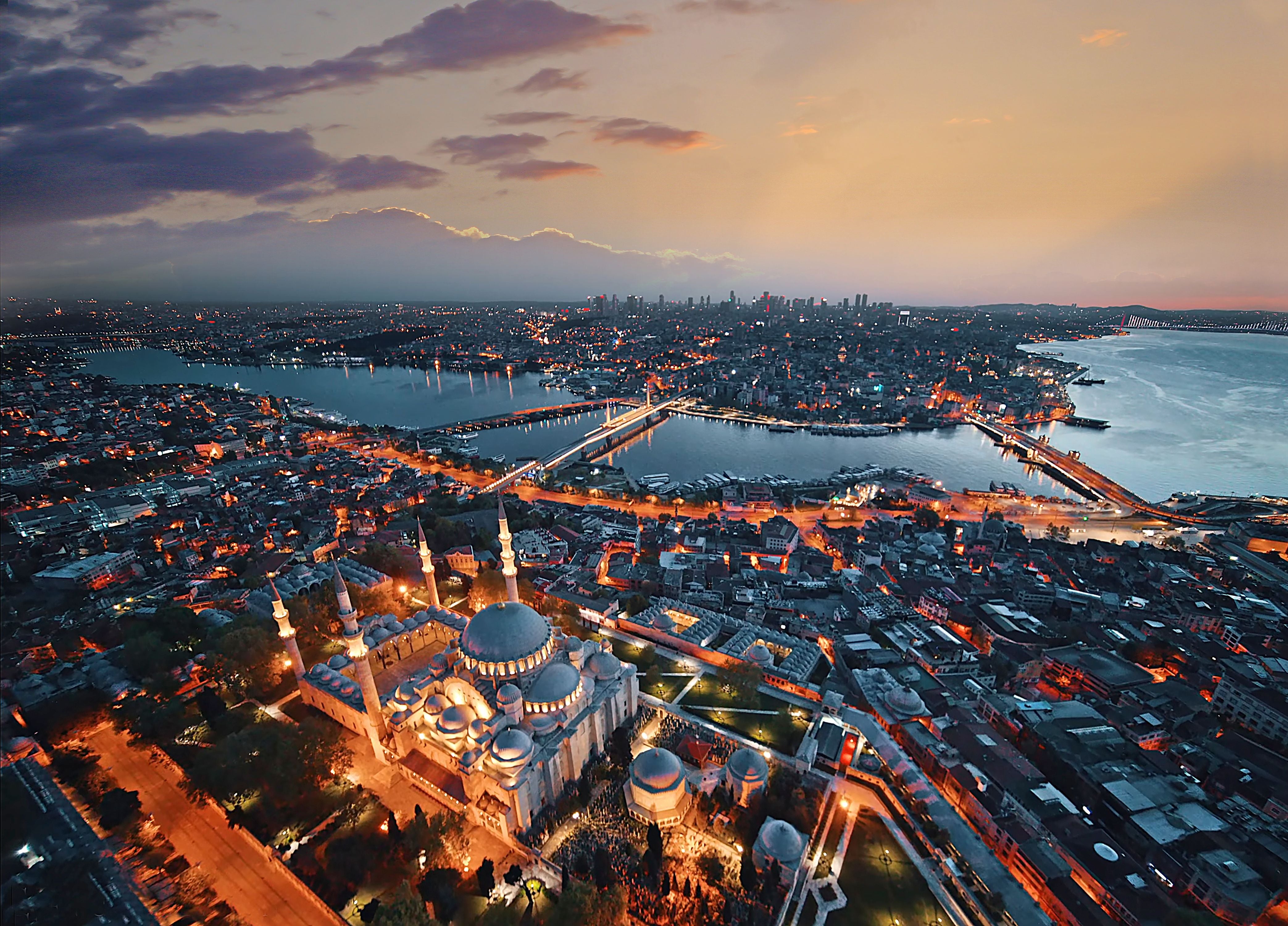 Luftaufnahme von Istanbul bei Nacht mit beleuchteter Moschee und Bosporus im Hintergrund.