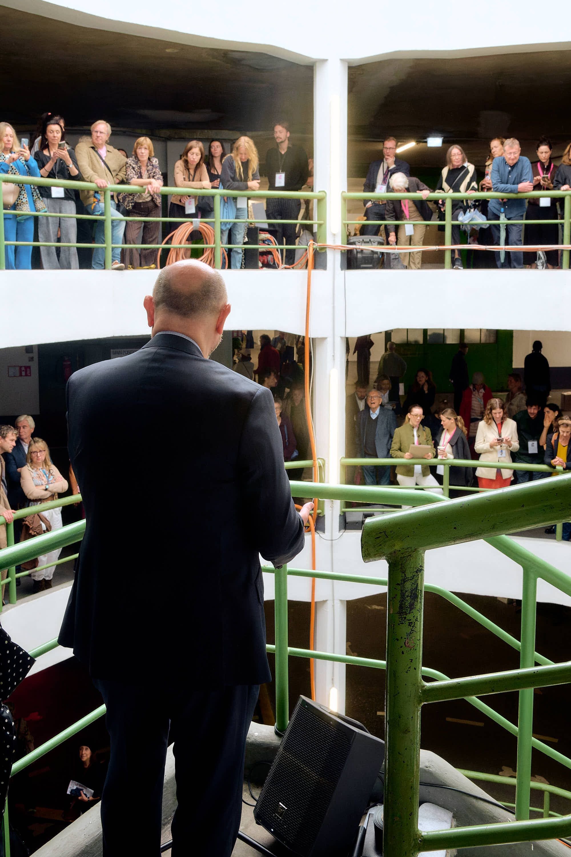Mann hält eine Rede bei der Eröffnung der Astoria Artshow, Publikum steht auf mehreren Ebenen.