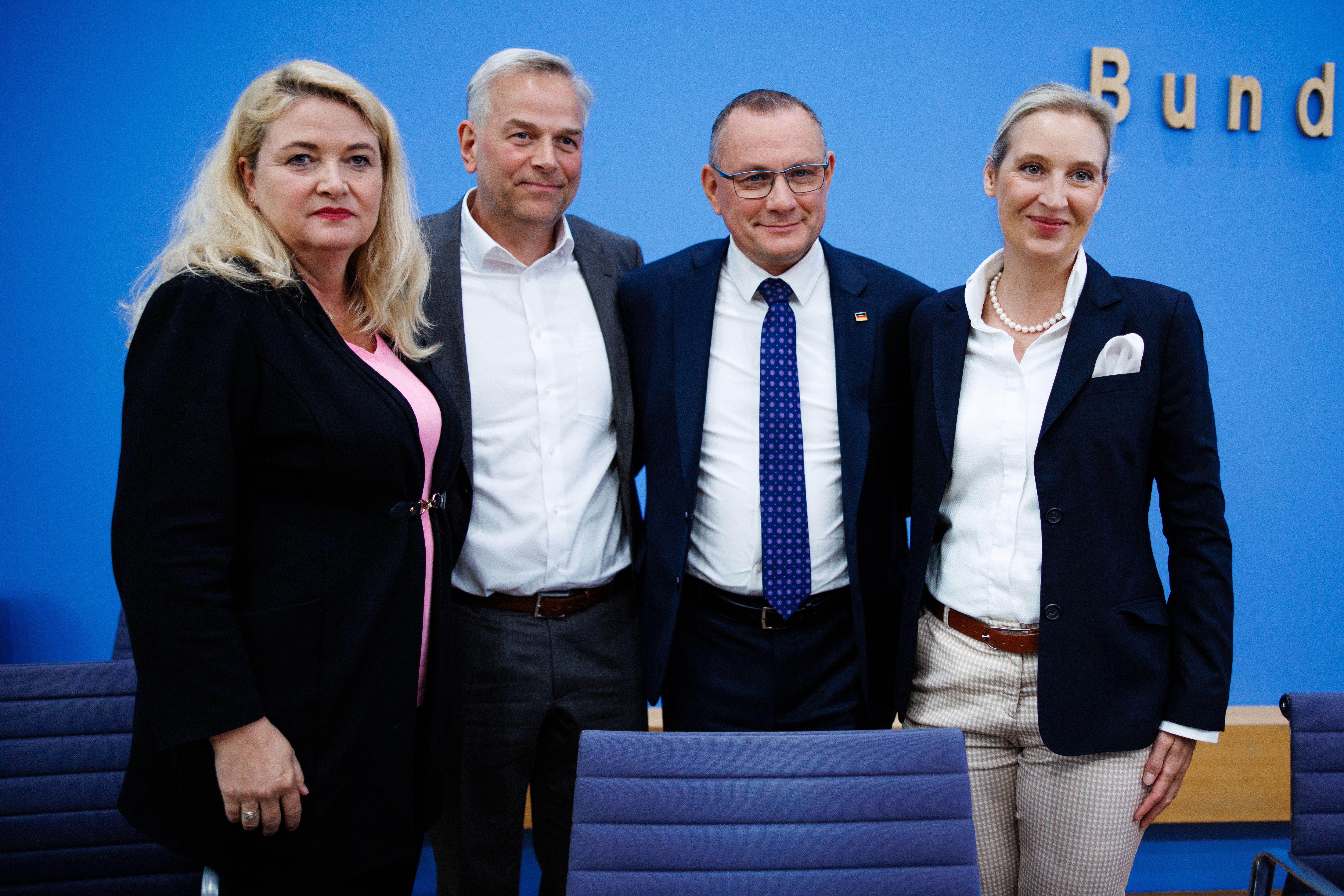 Vier Personen in Businesskleidung stehen vor einer blauen Wand und posieren für ein Gruppenfoto.