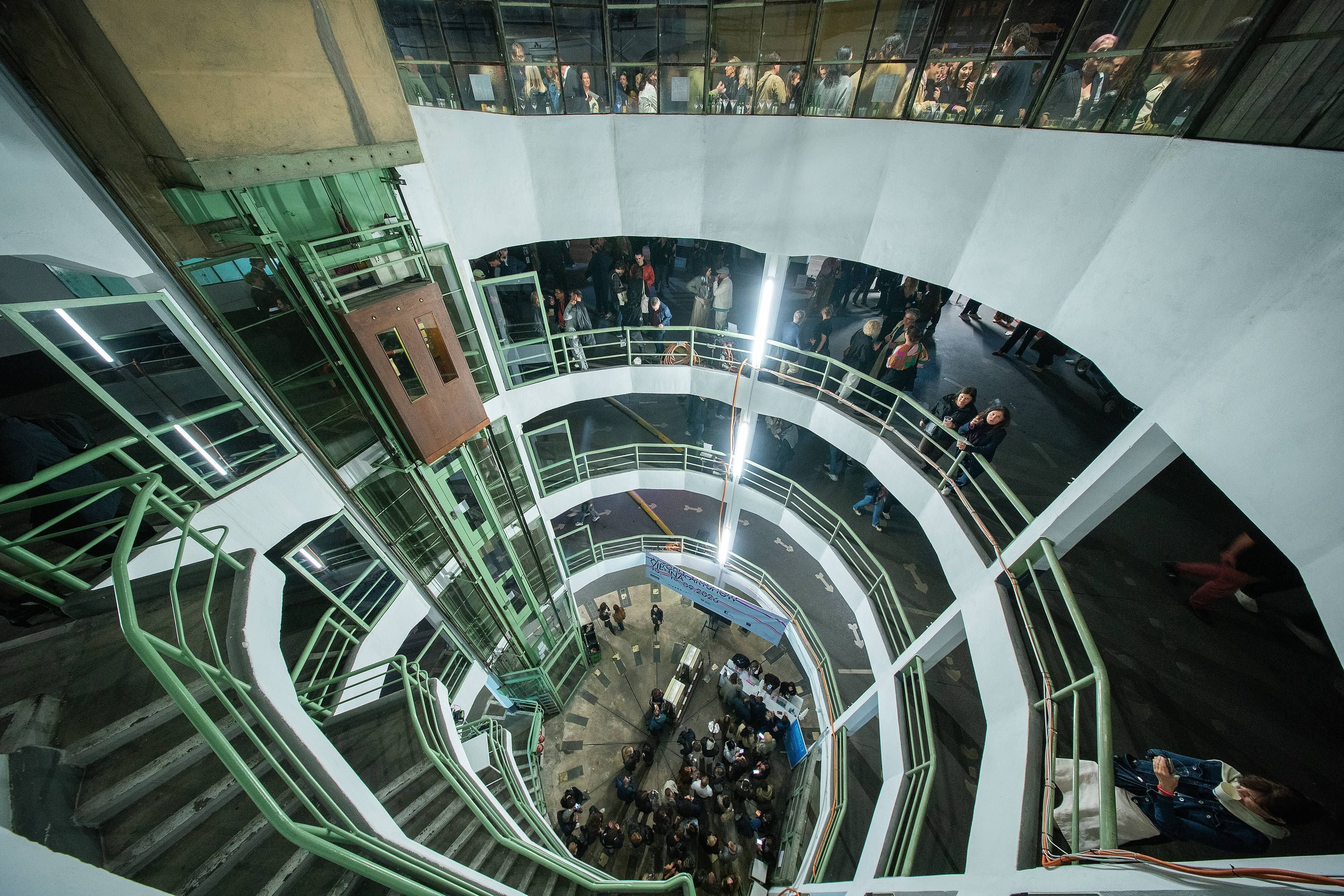 Blick in ein rundes Parkhaus mit grünen Geländern und vielen Menschen auf mehreren Ebenen.