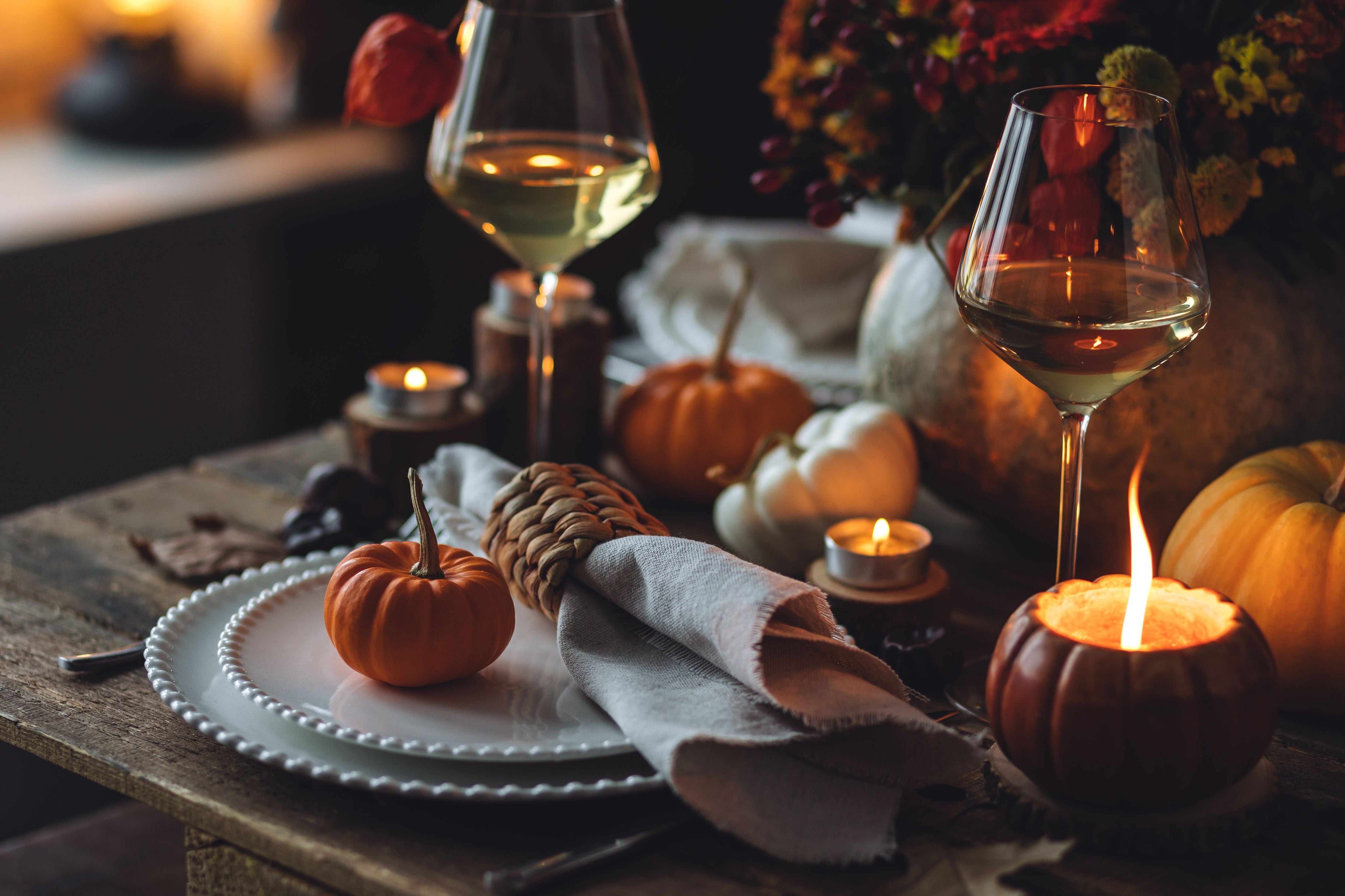Herbstlich dekorierter Tisch mit Wein, Kerzen, Kürbissen und elegantem Geschirr für ein festliches Dinner.