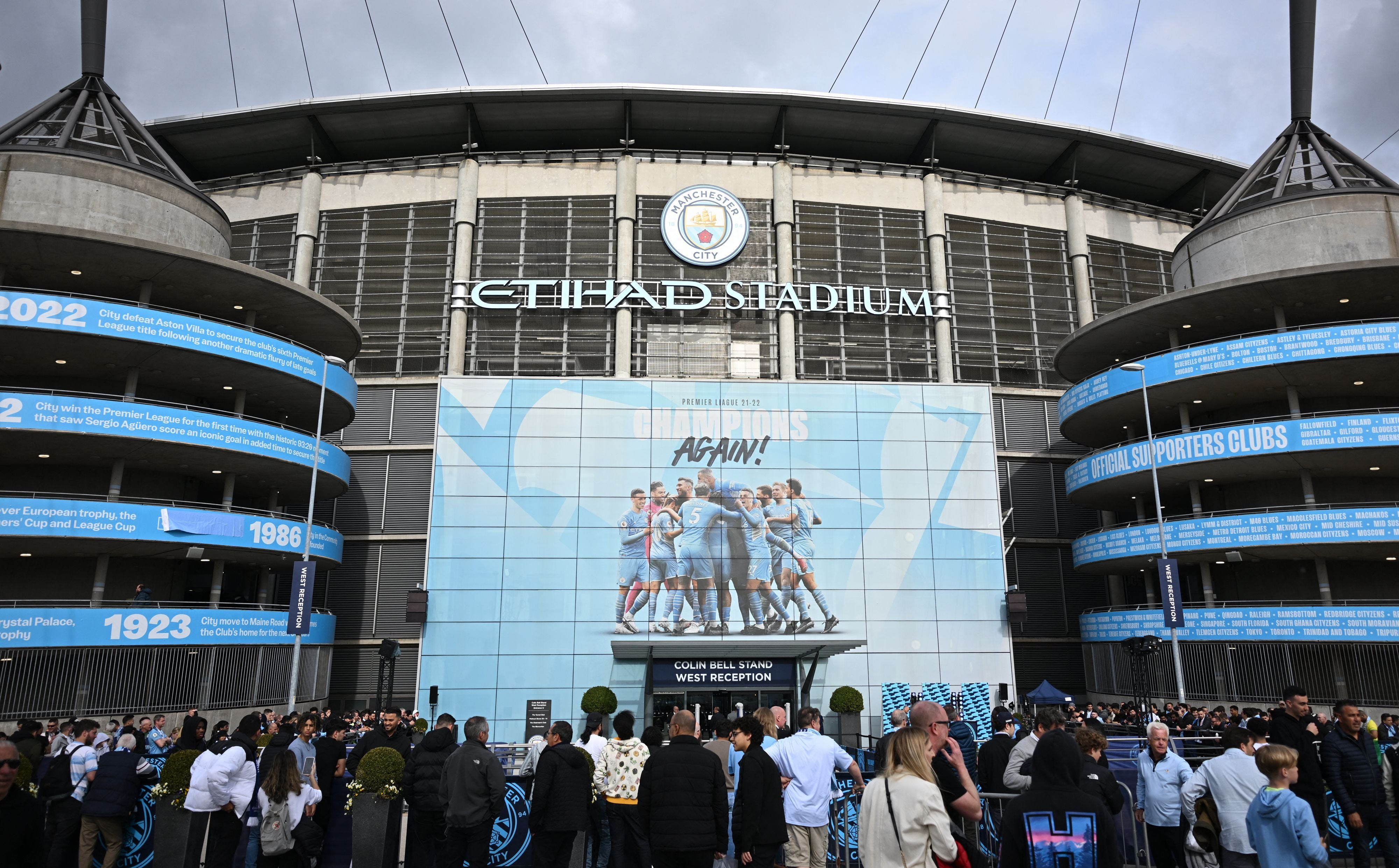 Die Außenfassade des Etihad Stadium in Manchester mit dem Vereinswappen und einem großen Plakat feiernder Spieler.