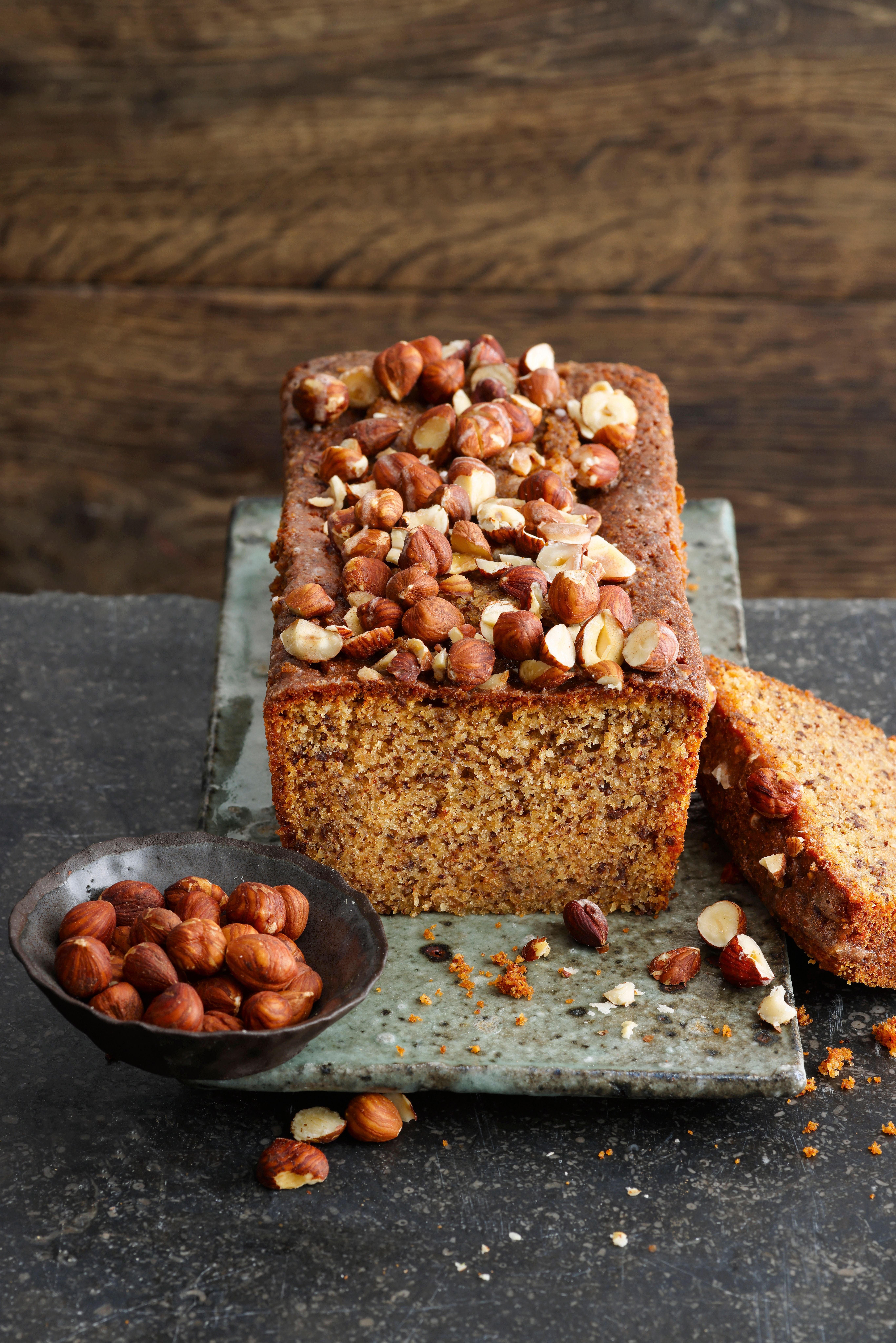 Schoko-Haselnuss-Kuchen mit Zimtguss, belegt mit ganzen Haselnüssen, daneben eine Schale Haselnüsse.
