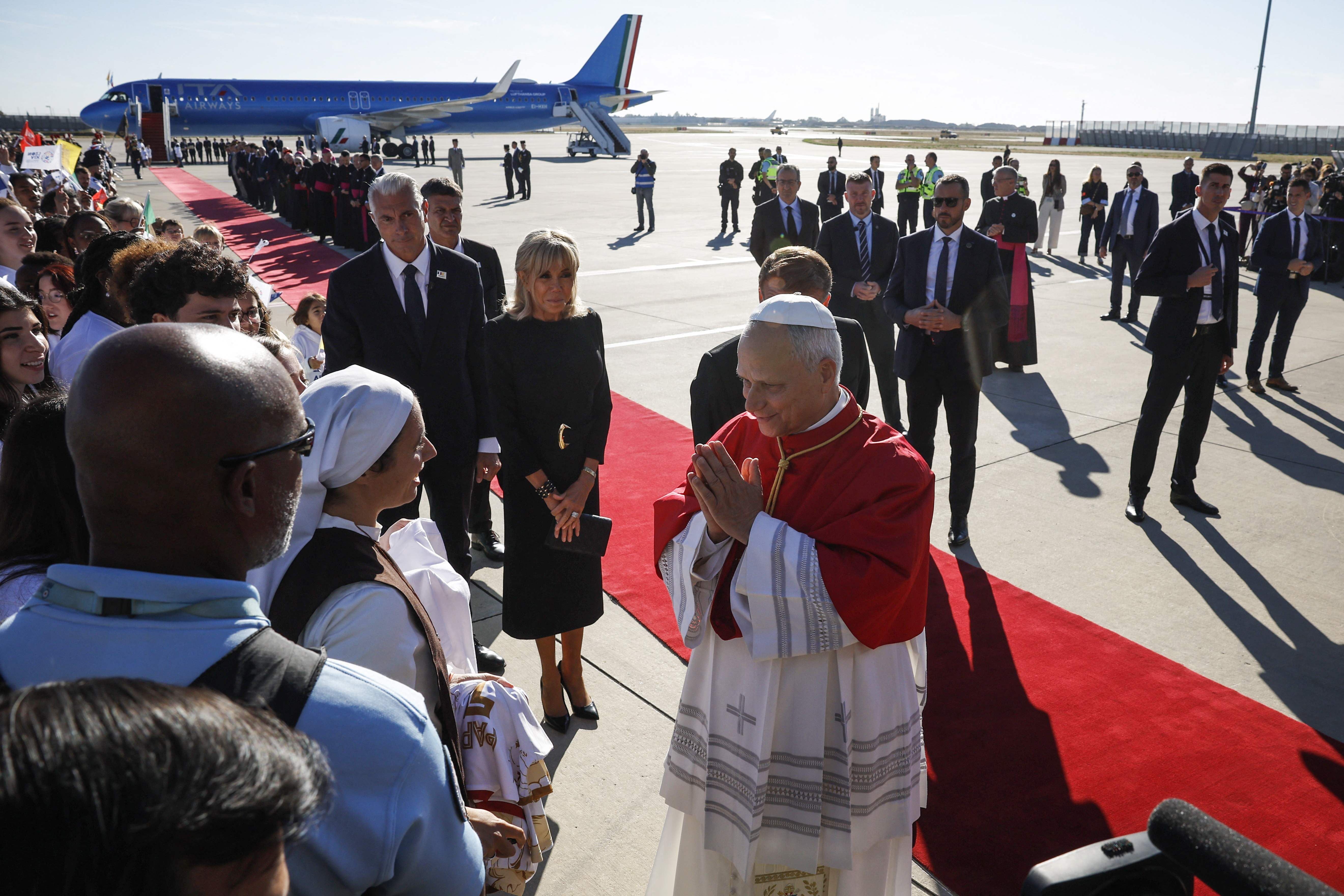 Papst Leo XIV. begrüßt am Flughafen Orly eine Nonne, umgeben von Sicherheitsleuten und Besuchern.
