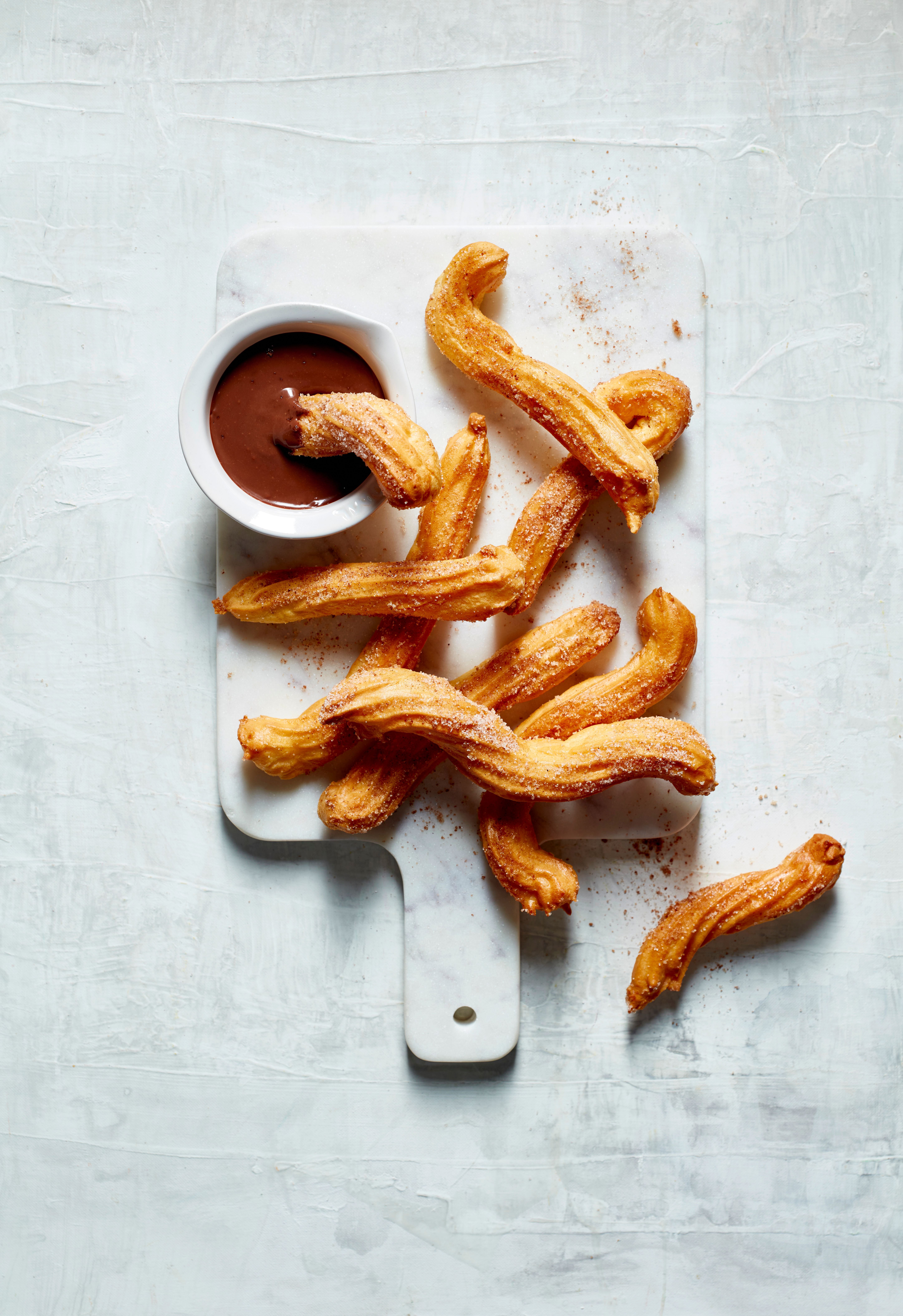 Frische Churros aus der Heißluftfritteuse mit Schokoladensauce auf einem weißen Brett.
