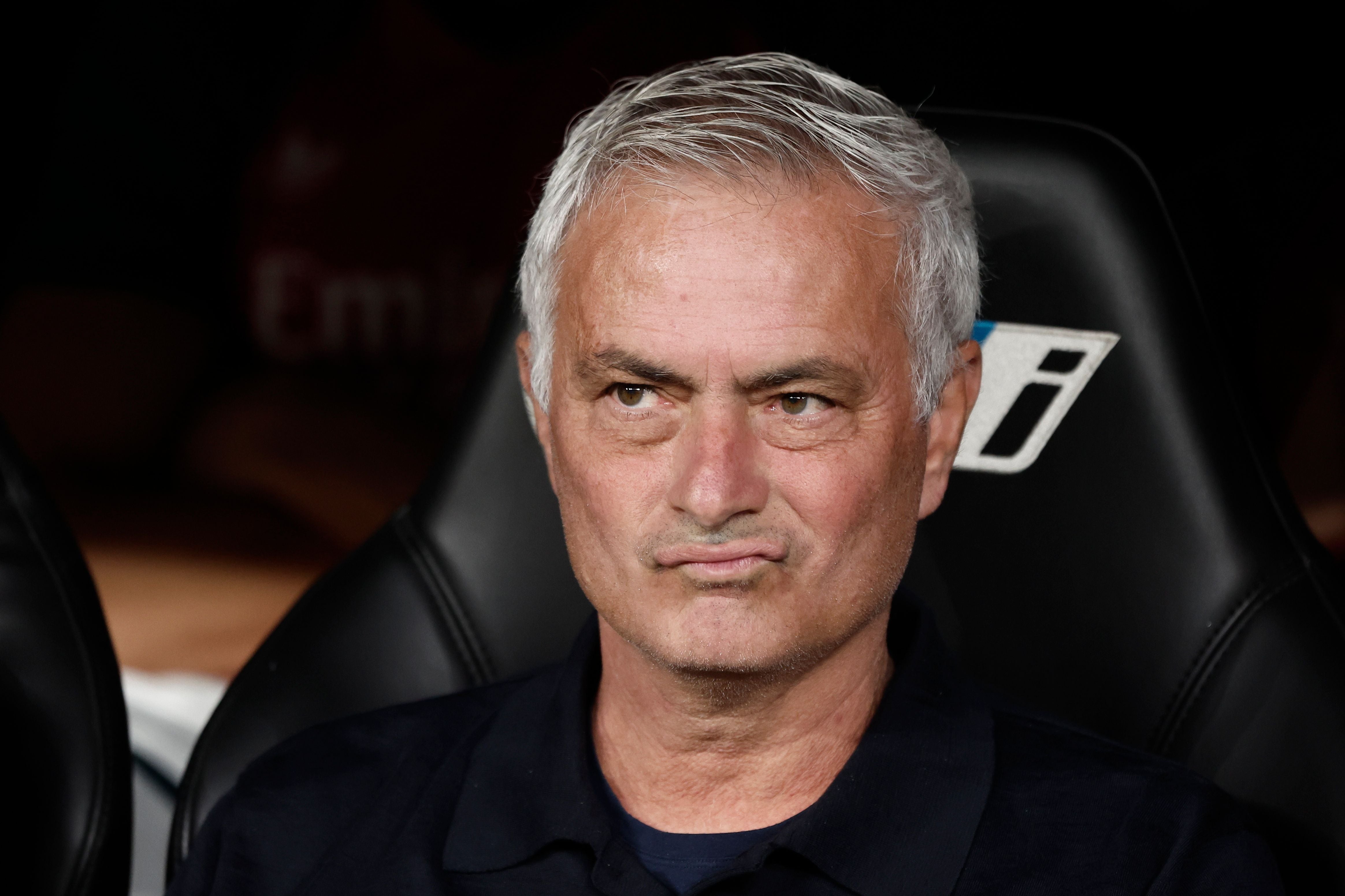 Jose Mourinho sitzt nachdenklich und mit skeptischem Blick auf der Trainerbank vor dem Markenlogo eines Sponsors.