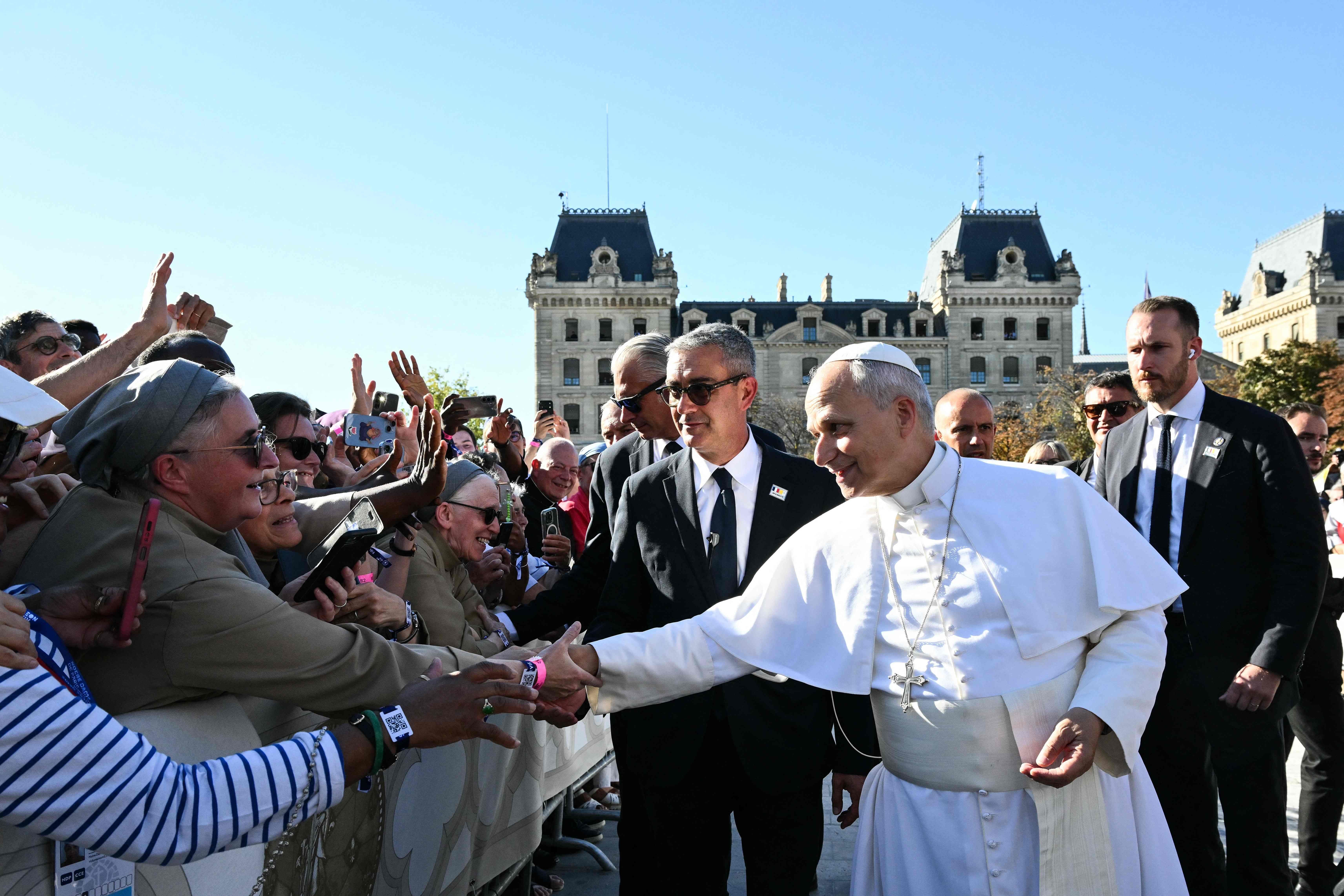 Ein Papst begrüßt eine jubelnde Menschenmenge vor einer Kathedrale bei sonnigem Wetter.