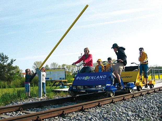 Mehrere Menschen fahren mit einer Draisine auf Gleisen bei sonnigem Wetter in Oberpullendorf.