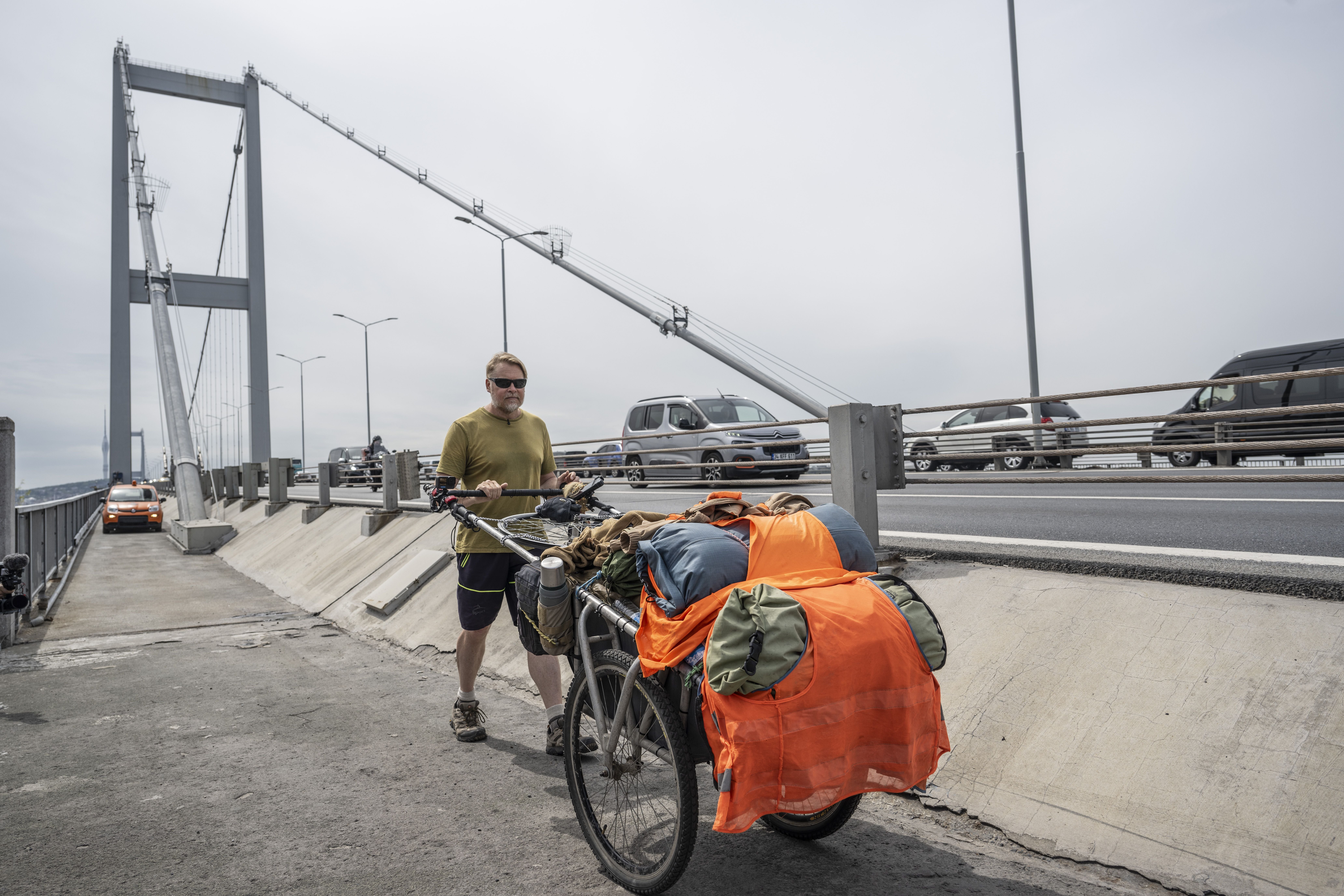 Ein Mann schiebt einen beladenen Wagen über eine große Brücke neben fahrendem Verkehr.
