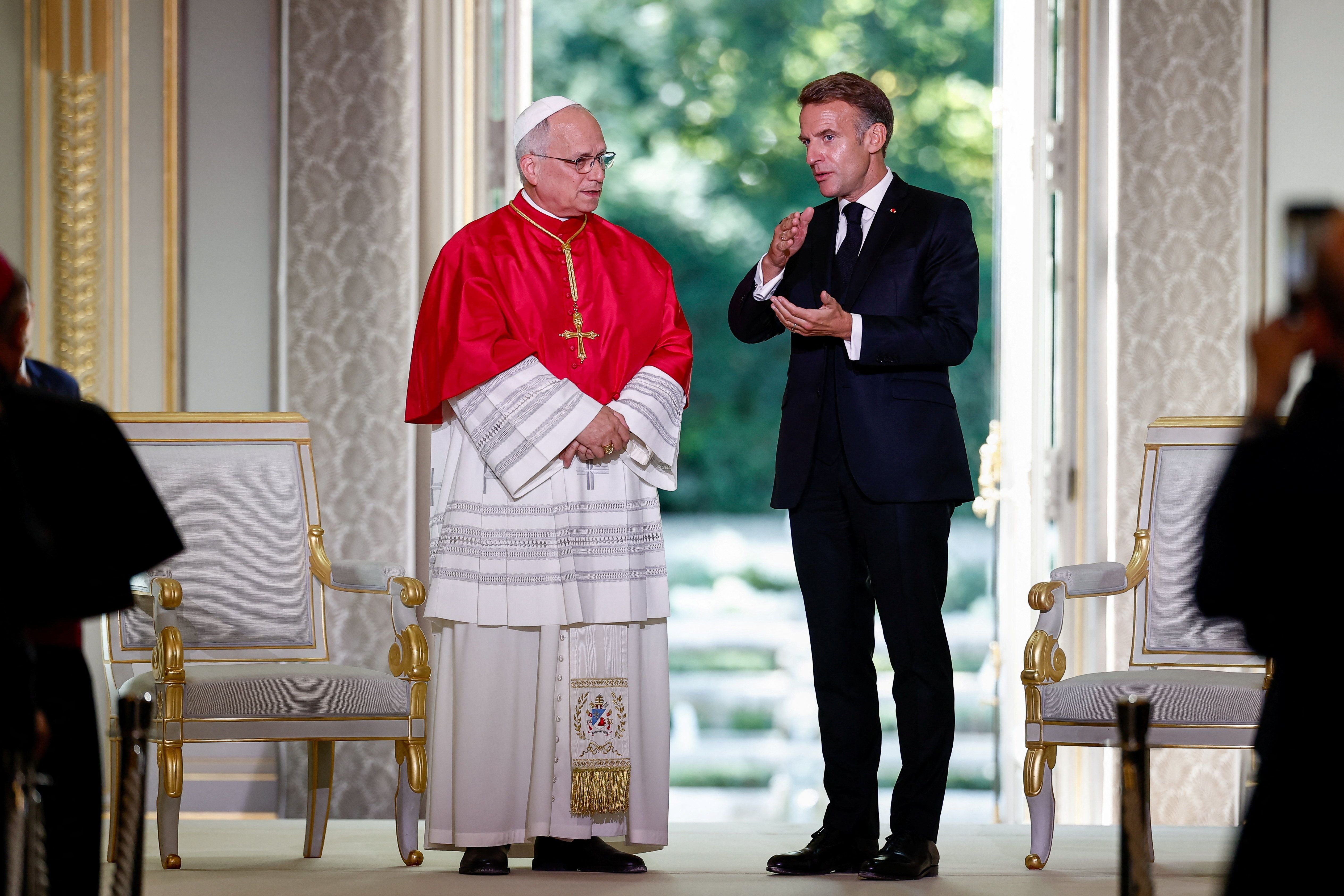 Ein Mann im Anzug spricht mit einem Kardinal in roter und weißer Robe in einem prunkvollen Raum.