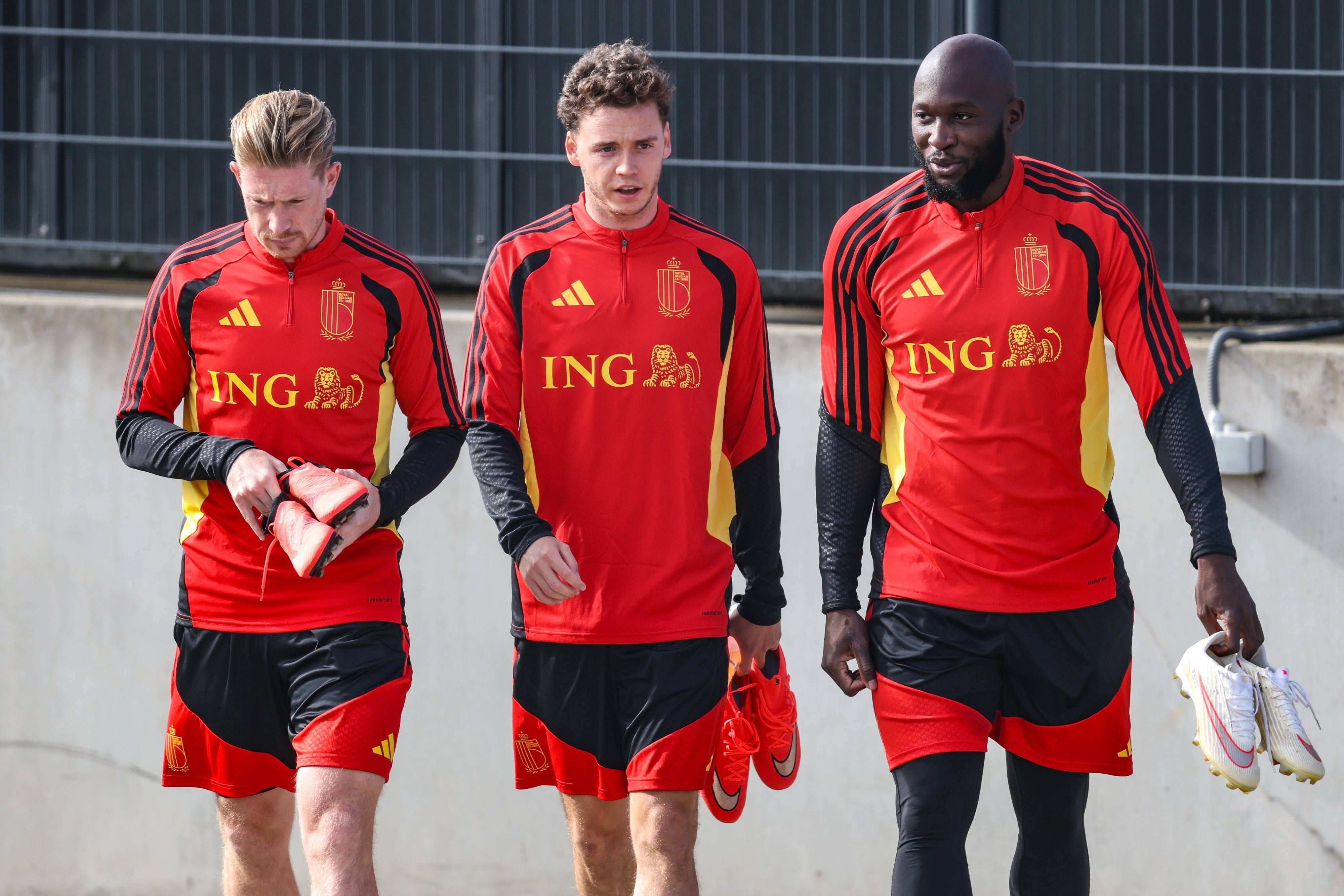Kevin De Bruyne, Mika Godts und Romelu Lukaku gehen im roten Trainingsanzug der belgischen Nationalmannschaft nebeneinander über den Platz.