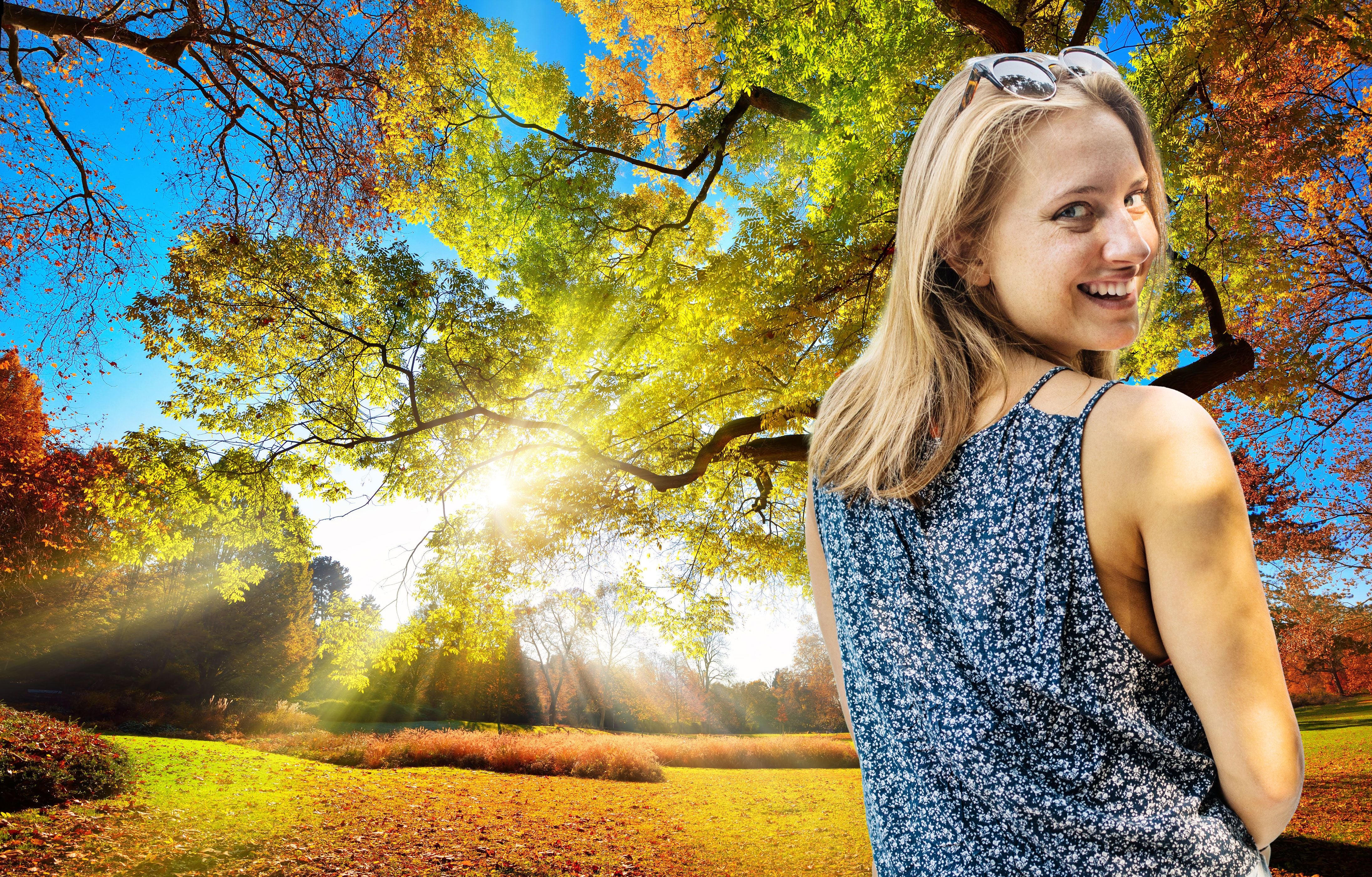 Junge Frau lächelt im herbstlichen Park bei Sonnenschein und buntem Blätterdach.