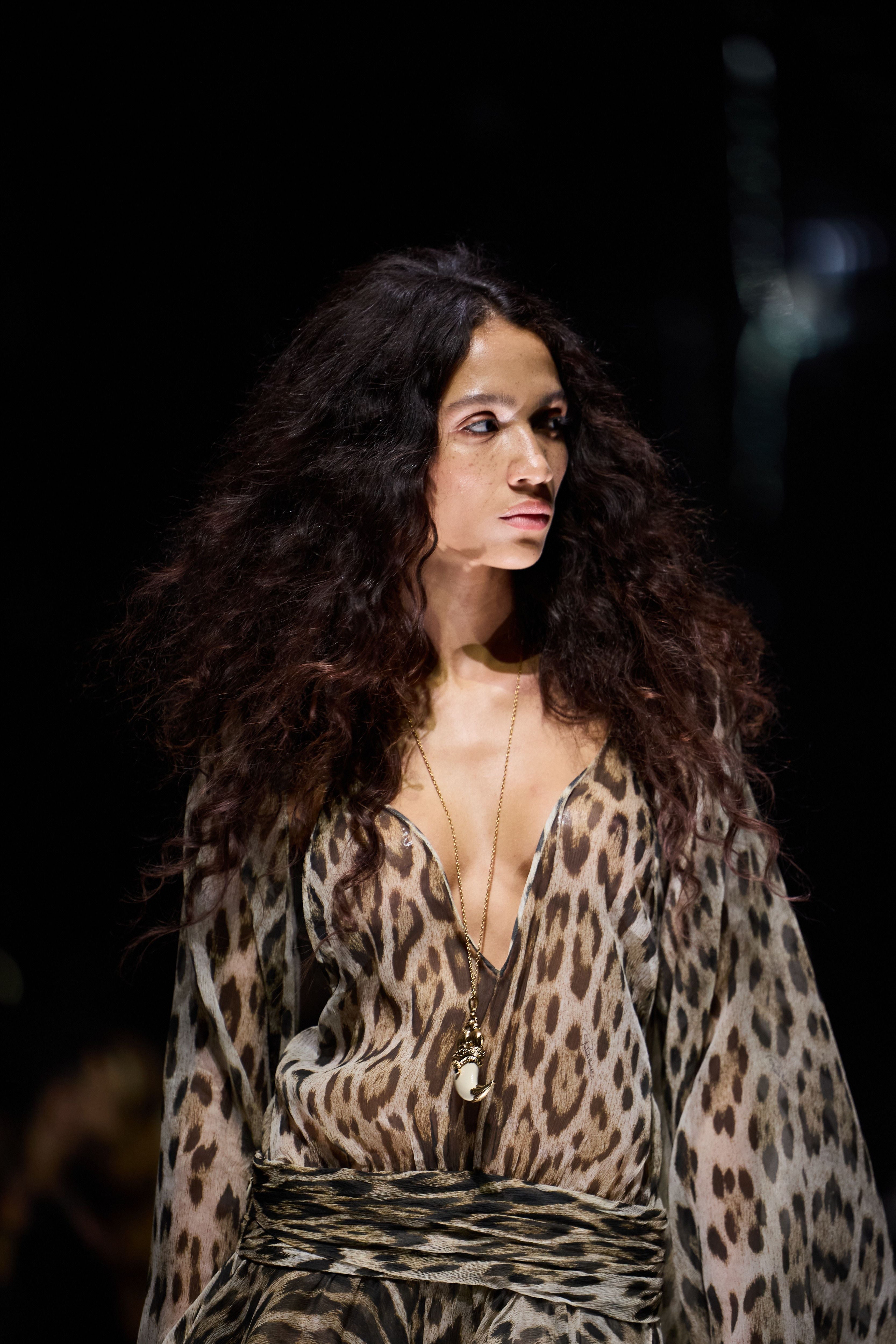 Model mit langen, lockigen Haaren trägt ein Kleid mit Leopardenmuster auf dem Laufsteg.