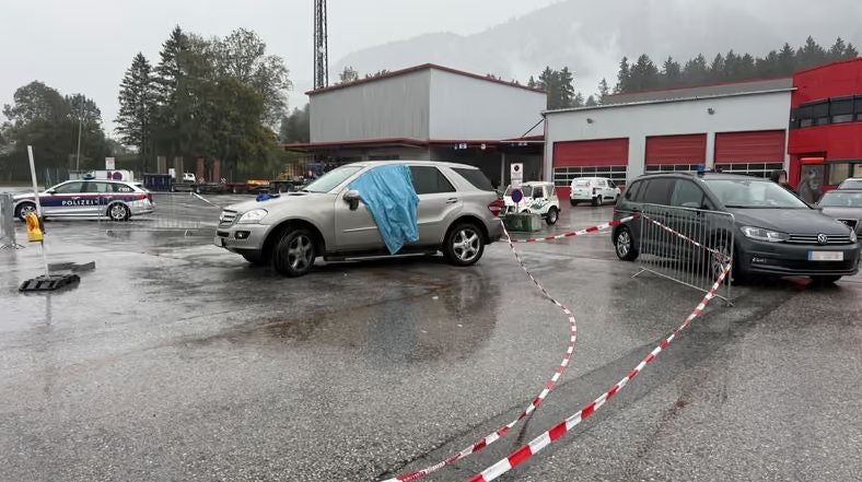 Polizeiautos und Absperrband sichern einen regennassen Parkplatz mit abgedecktem SUV in Radfeld.