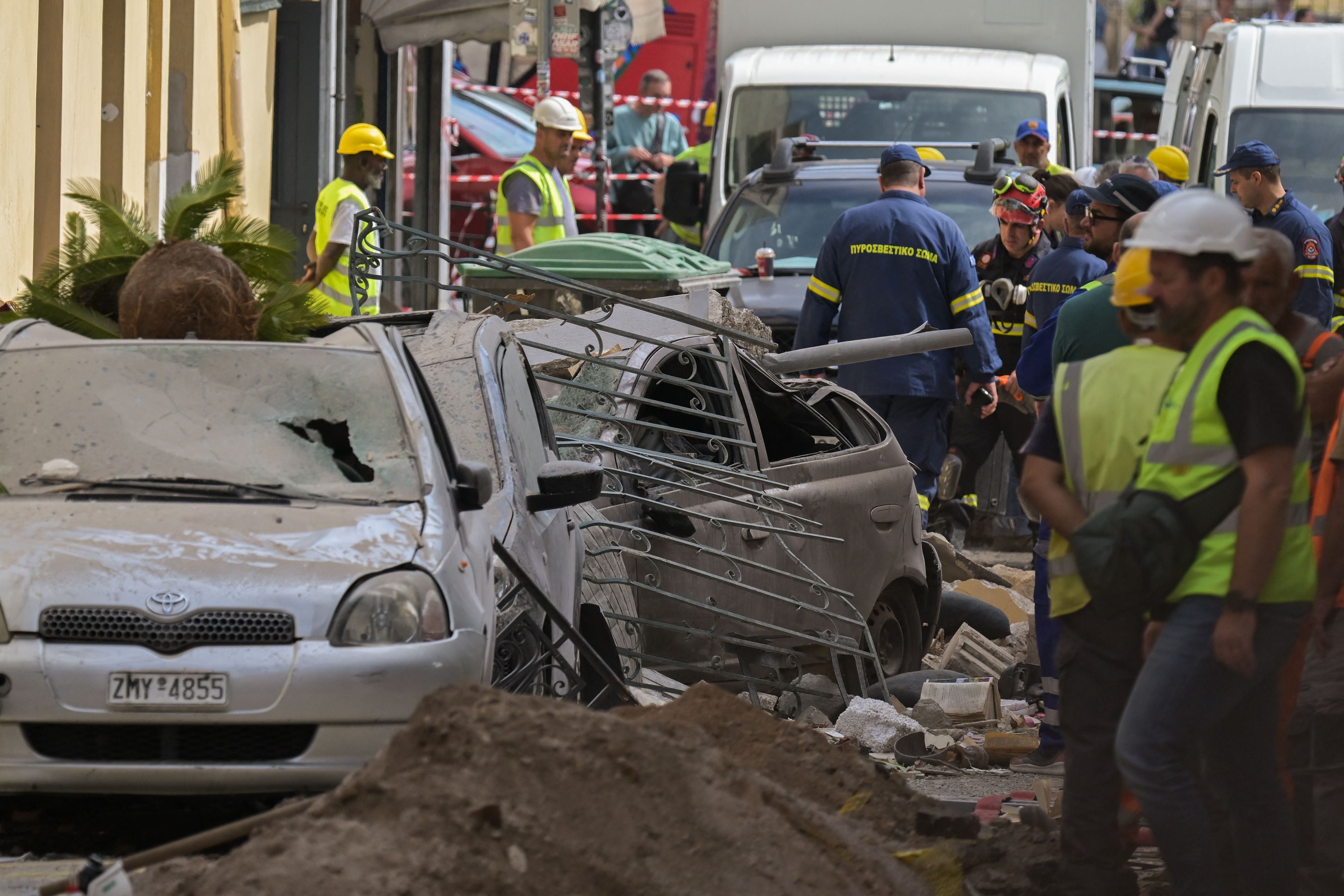 Einsatzkräfte sichern ein zerstörtes Auto an einer eingestürzten Hauswand in Athen.