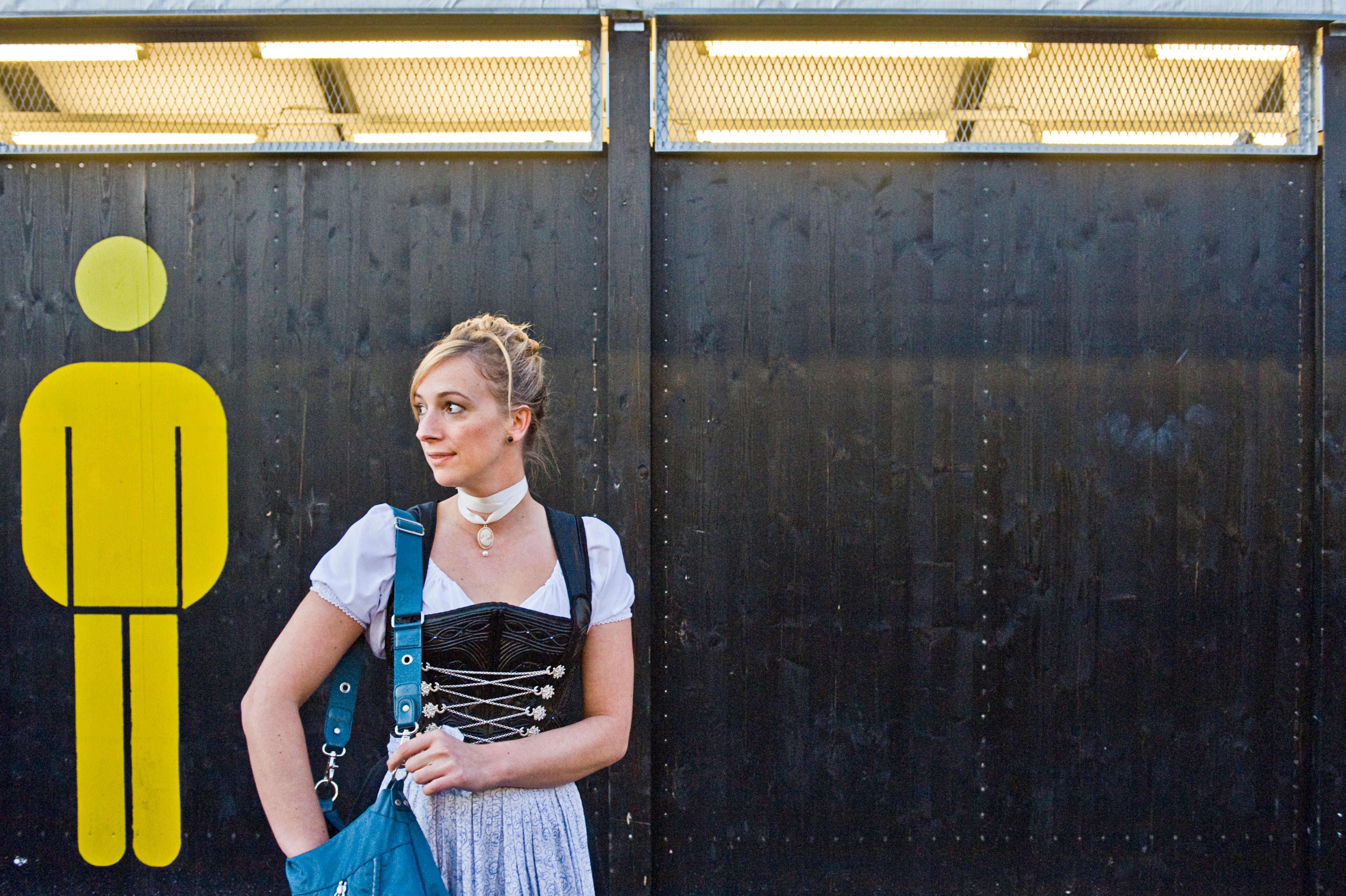 Frau in Dirndl steht vor einem Toilettenschild auf dem Oktoberfest.