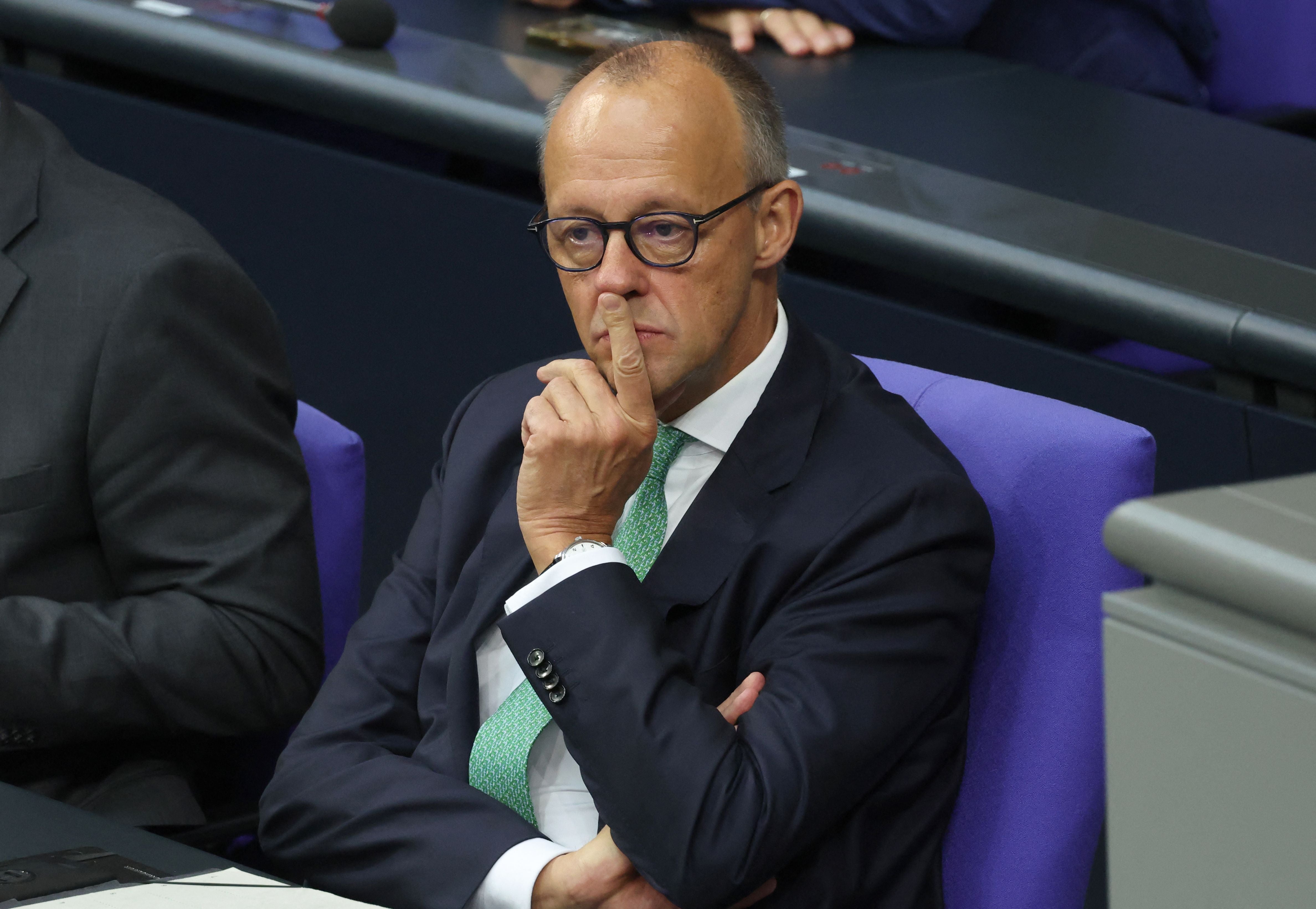 Ein Mann im Anzug sitzt nachdenklich mit verschränkten Armen im Bundestag auf einem lila Stuhl.
