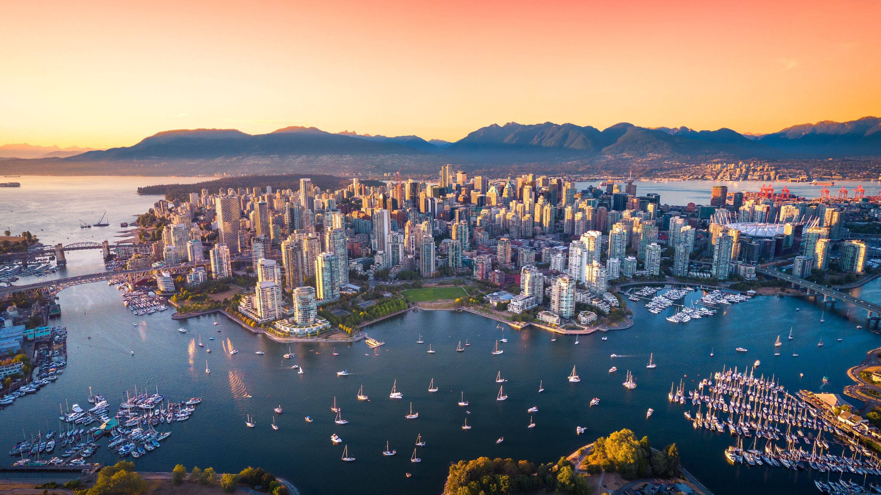 Luftaufnahme der Skyline von Vancouver bei Sonnenuntergang mit vielen Segelbooten im Wasser.