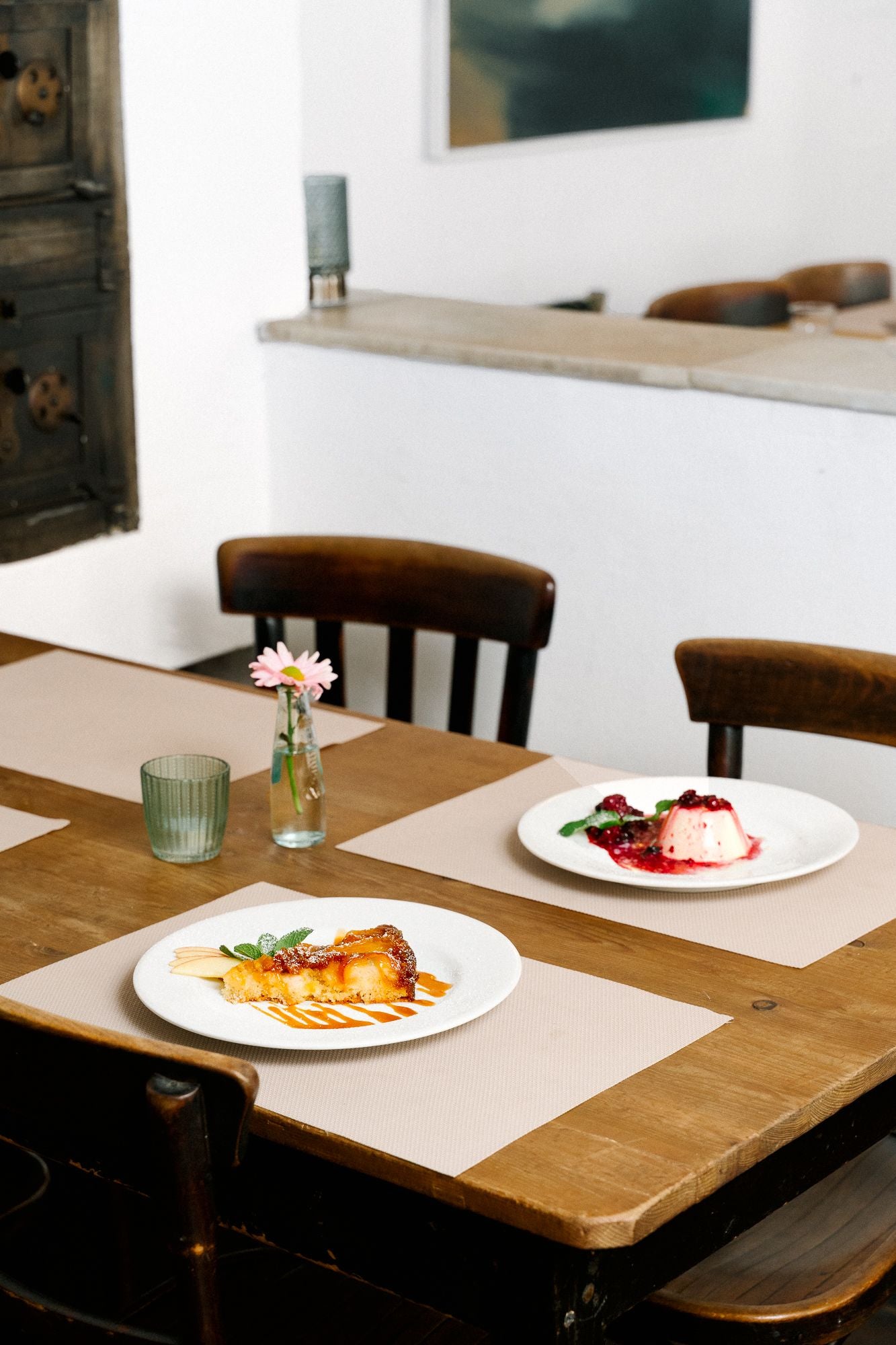 Zwei Teller mit Dessert stehen auf einem gedeckten Holztisch in einem gemütlichen Restaurant.