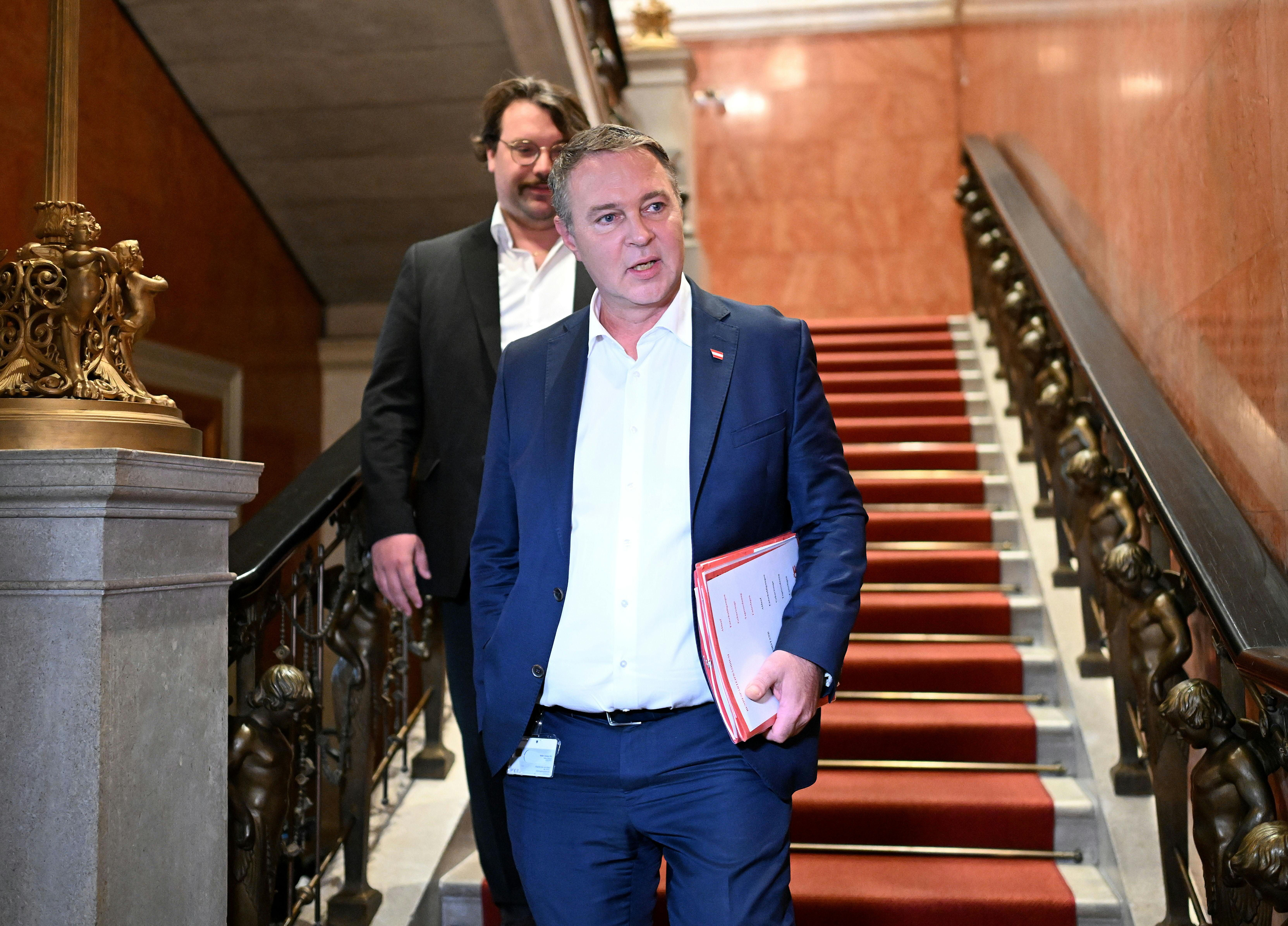 Ein Mann im Anzug geht mit Unterlagen eine prunkvolle Treppe mit rotem Teppich hinunter.