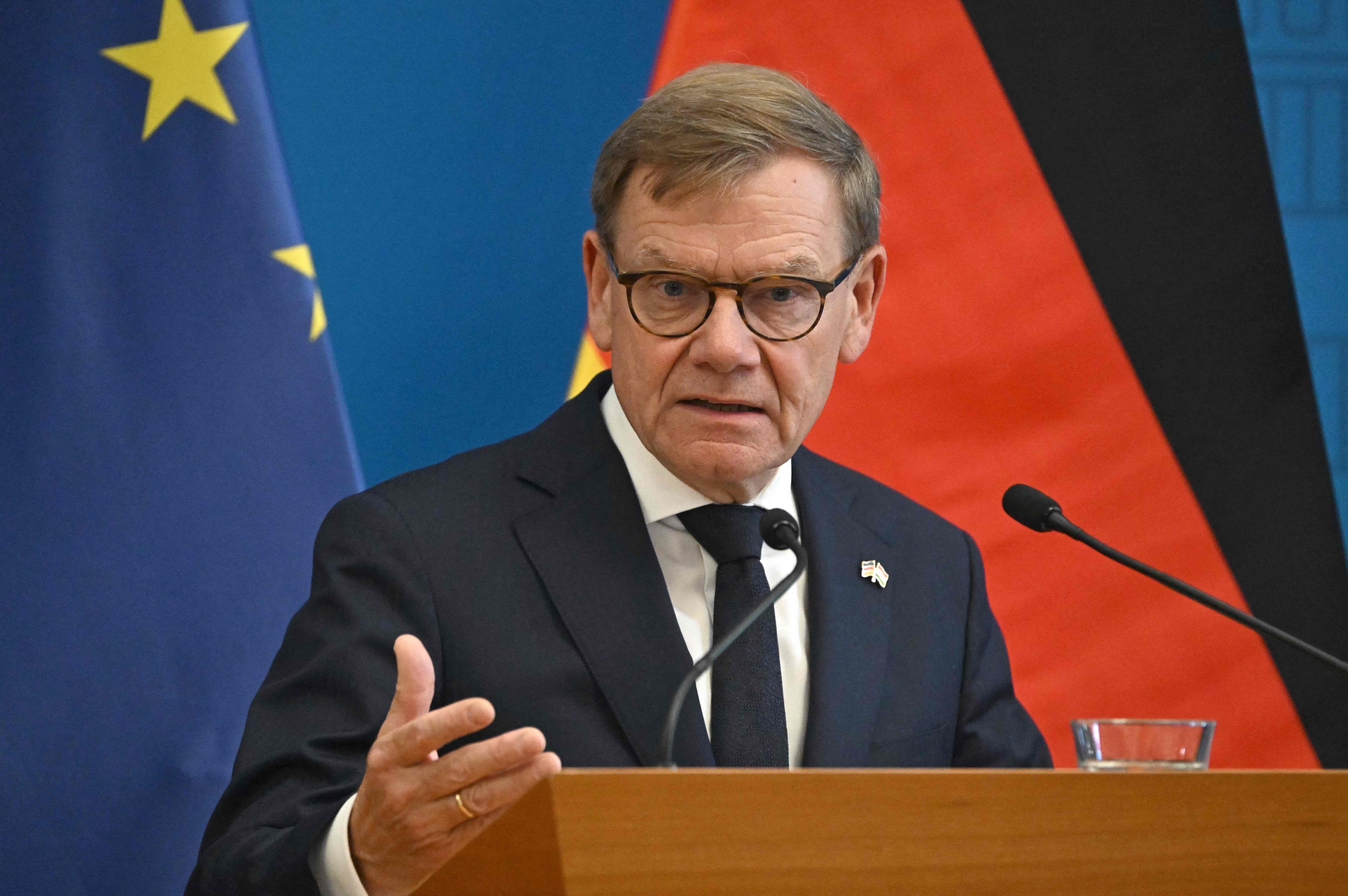 Ein Mann im Anzug spricht bei einer Pressekonferenz vor EU- und Deutschlandflagge.