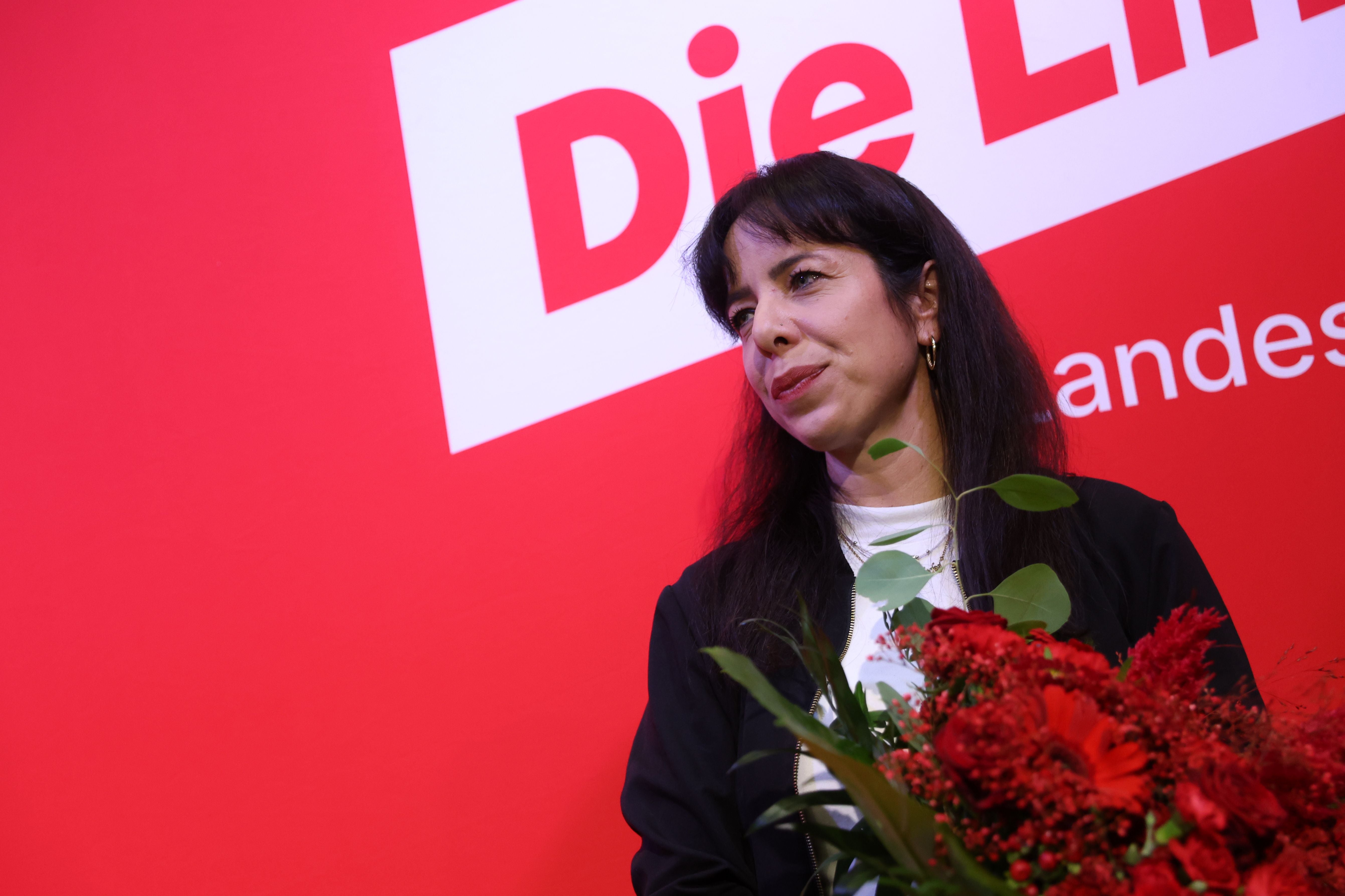 Frau mit Blumenstrauß vor rotem Hintergrund mit "Die Linke"-Logo.