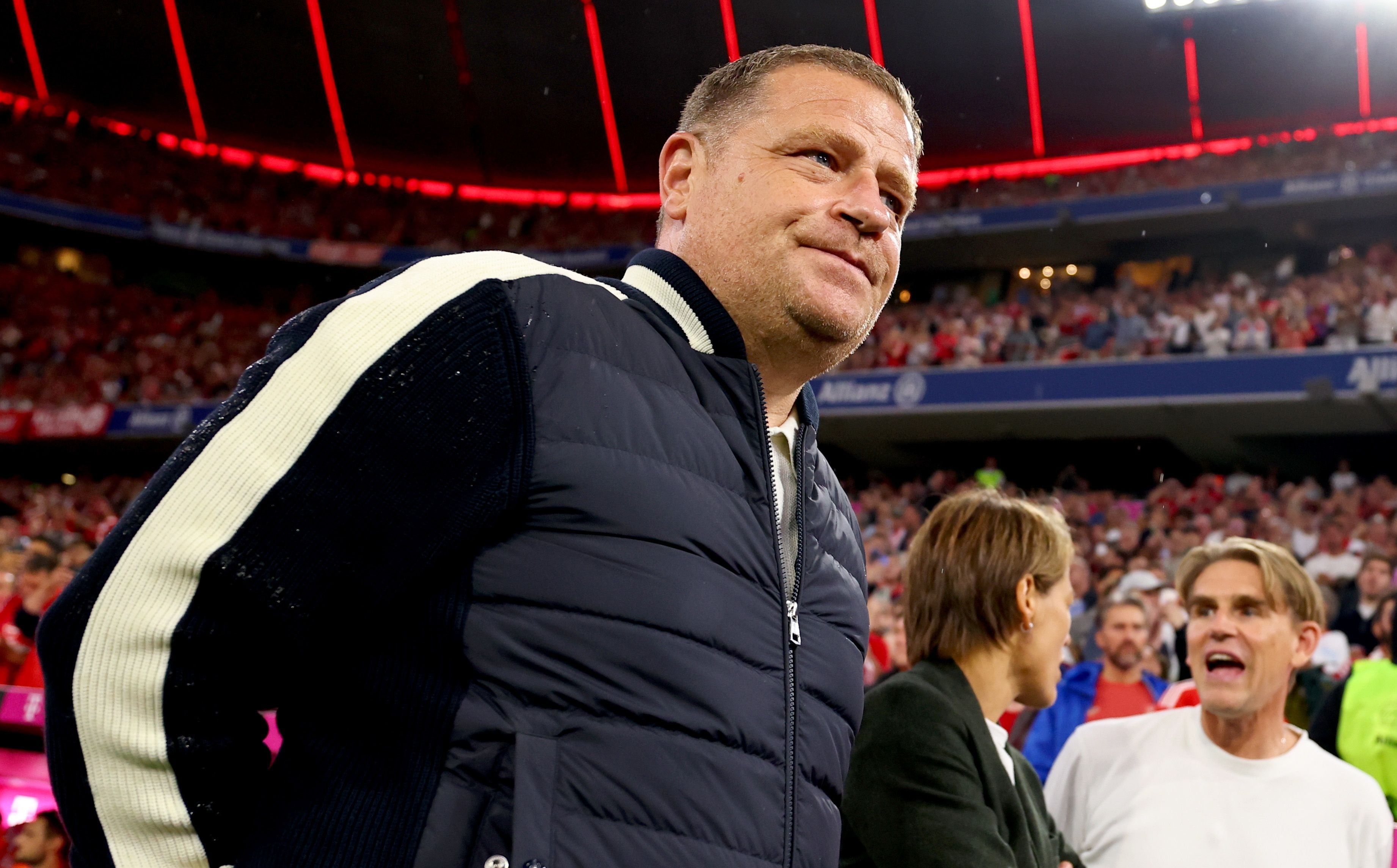 Ein Mann steht in einem Stadion, im Hintergrund jubelnde Fußballfans.