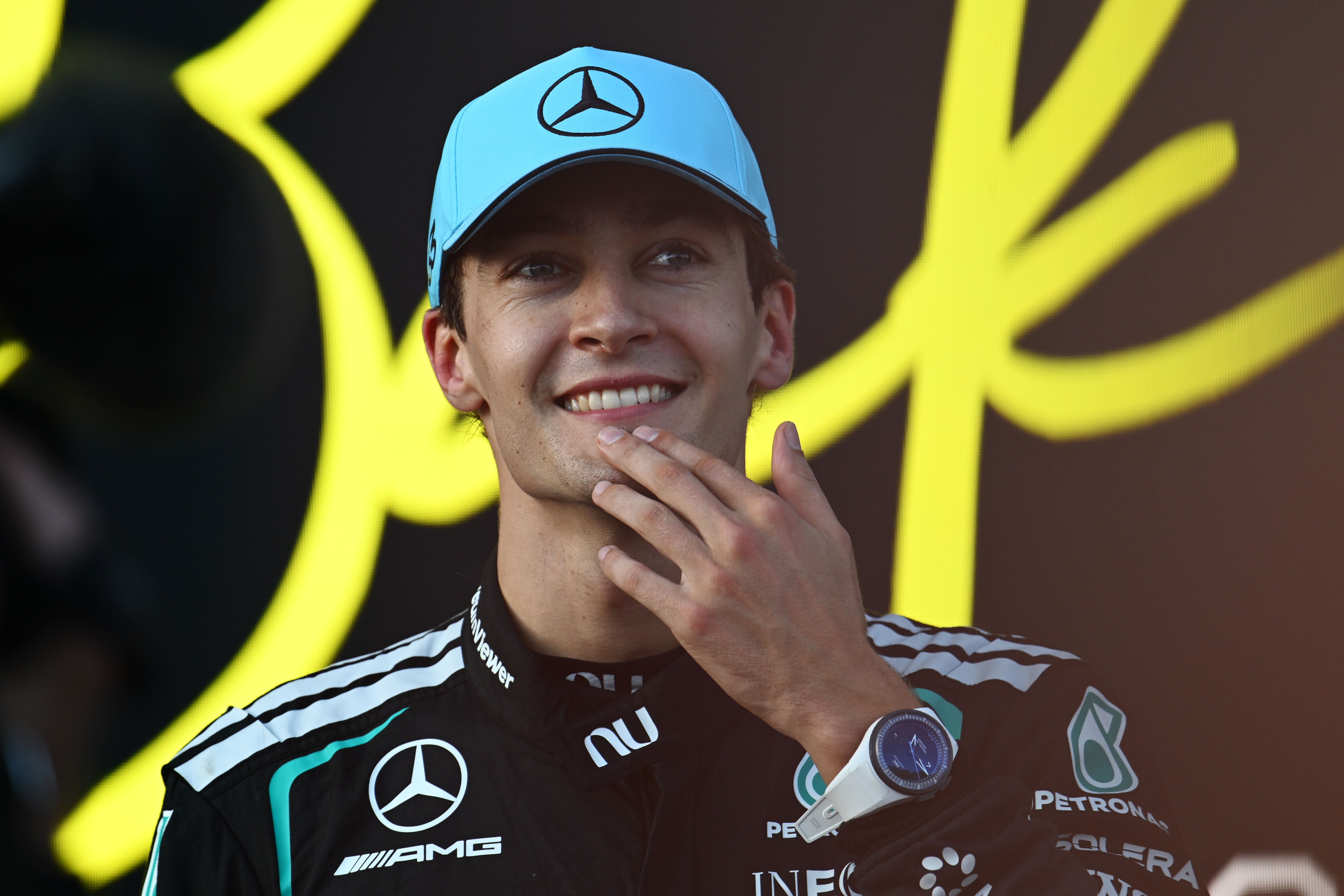 Ein Rennfahrer in Mercedes-Montur lächelt und trägt eine blaue Kappe mit Mercedes-Logo.